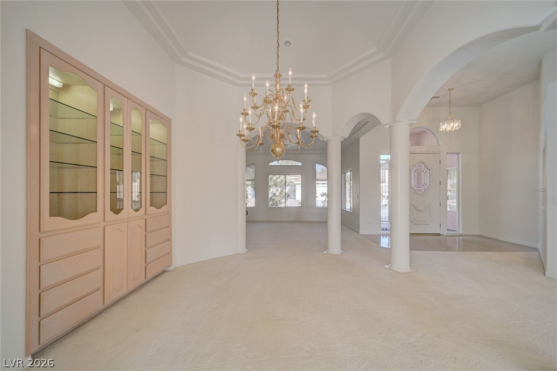 Vacant formal dining area with an ornate chandelier, glass-front built-in cabinetry, and arched columns.