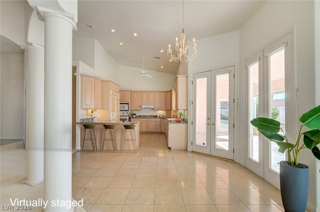 Open kitchen with raised breakfast bar, vaulted ceiling, chandelier, and glass doors to a patio.