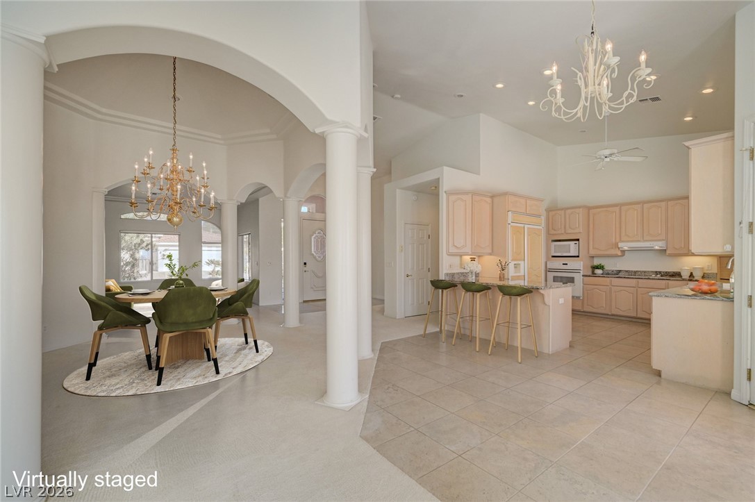 Open-plan dining room and kitchen with green chairs, arched openings, columns, and a breakfast island.