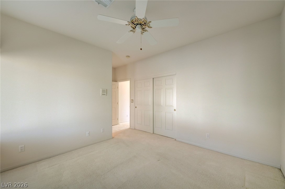 Empty bedroom with carpet, double closet doors, and a ceiling fan.