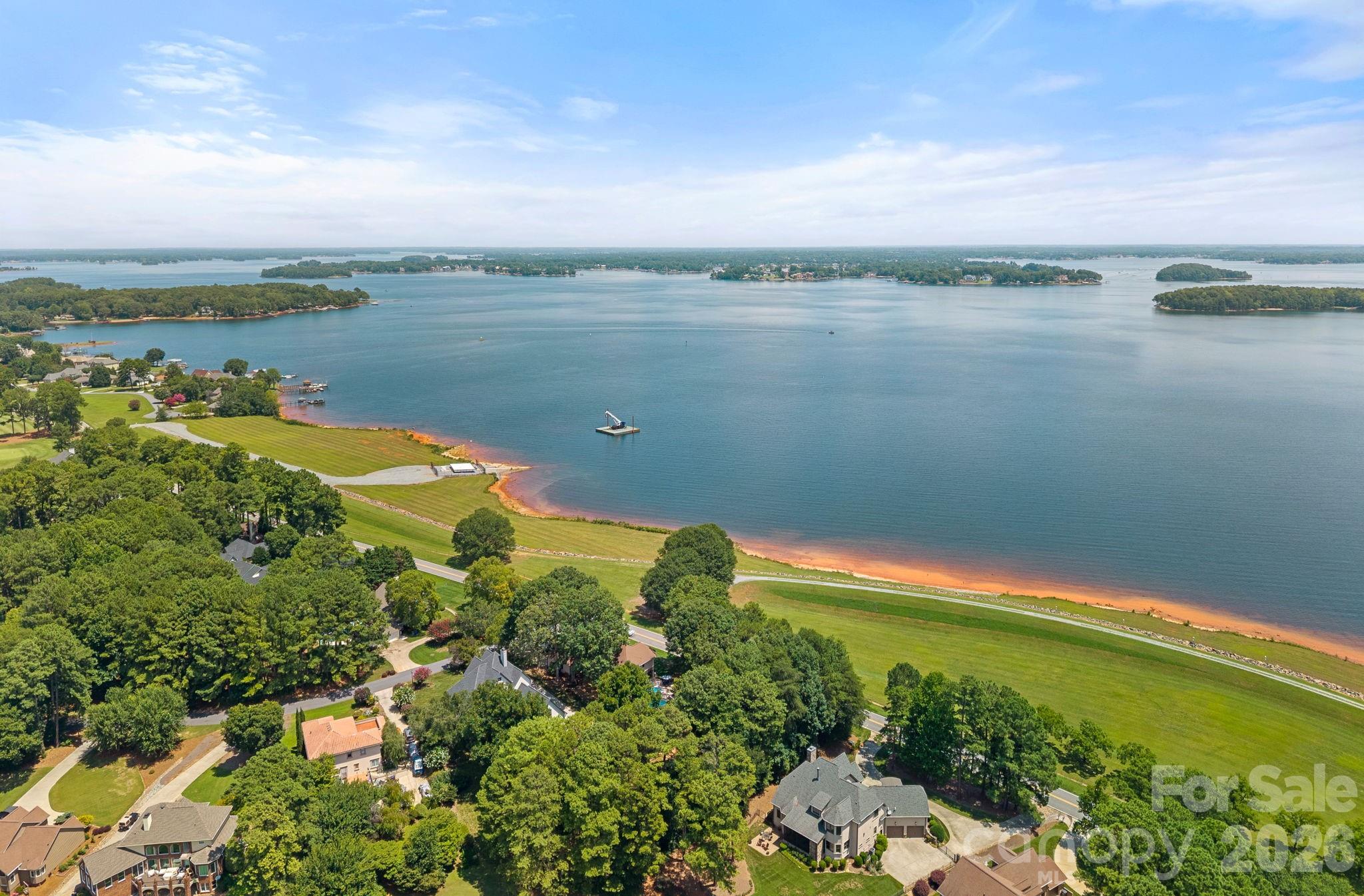 Aerial view of a lake and wooded islands, with waterfront homes and a broad green shoreline.