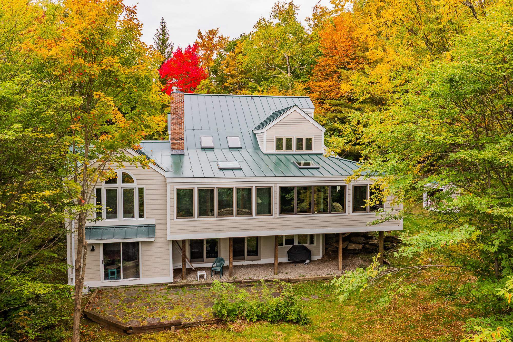 Multi-level beige home with a metal roof nestled among vivid autumn trees.