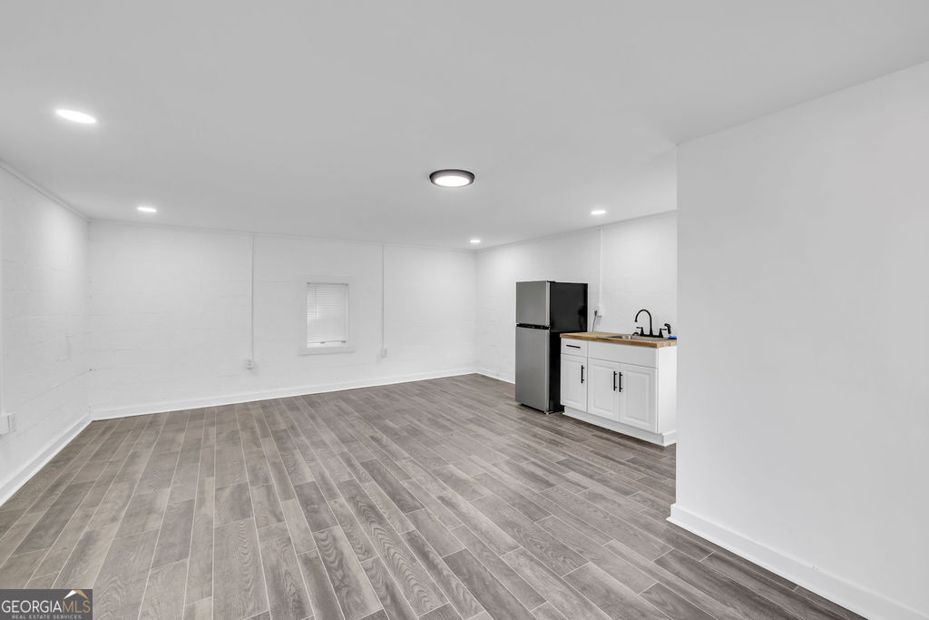 Vacant room with gray tile flooring and a compact kitchenette along the back wall.