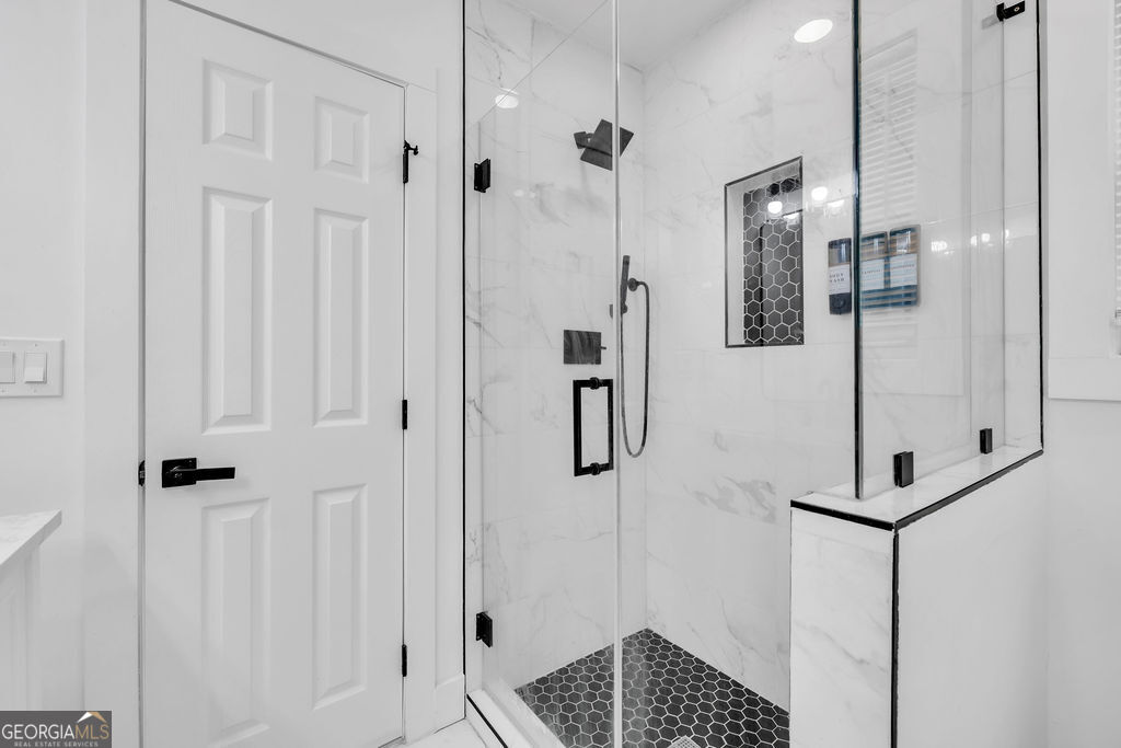 Bathroom shower with glass enclosure, marble-look tile, dark hexagonal floor, and black fixtures.