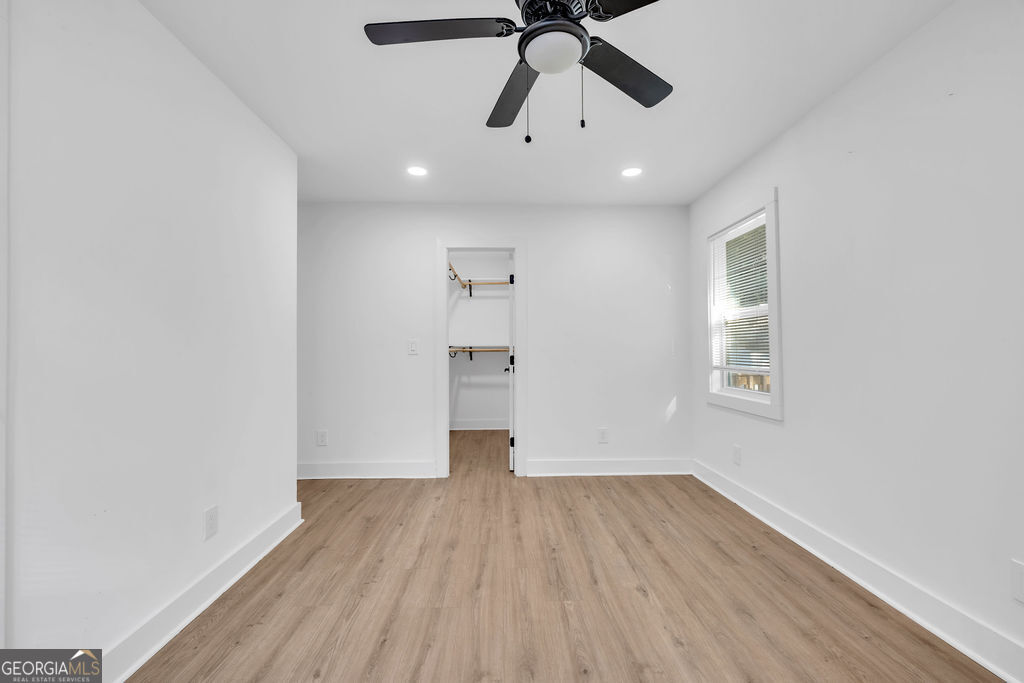 Unfurnished bedroom with a ceiling fan, wood-look flooring, and an open closet.