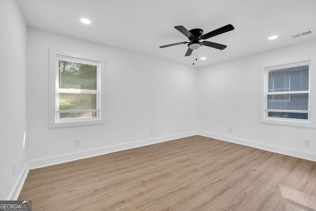 Empty room with wood-look flooring, two windows, and a black ceiling fan.