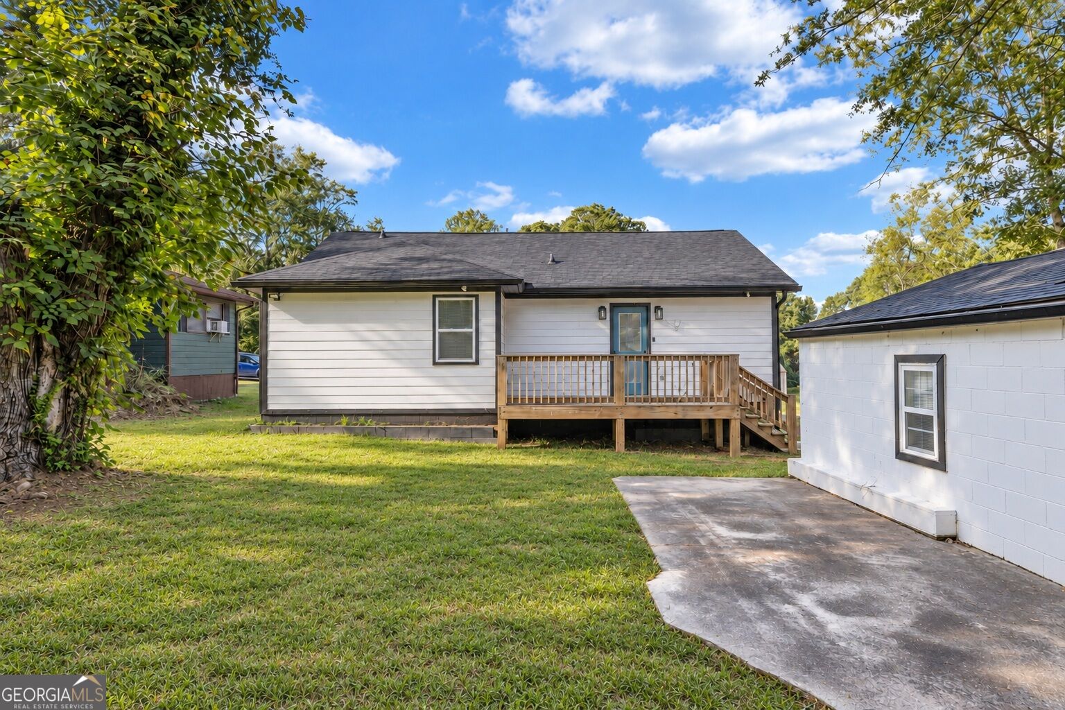 Rear of a white single-story house with a raised wooden deck, lawn, and concrete patio.