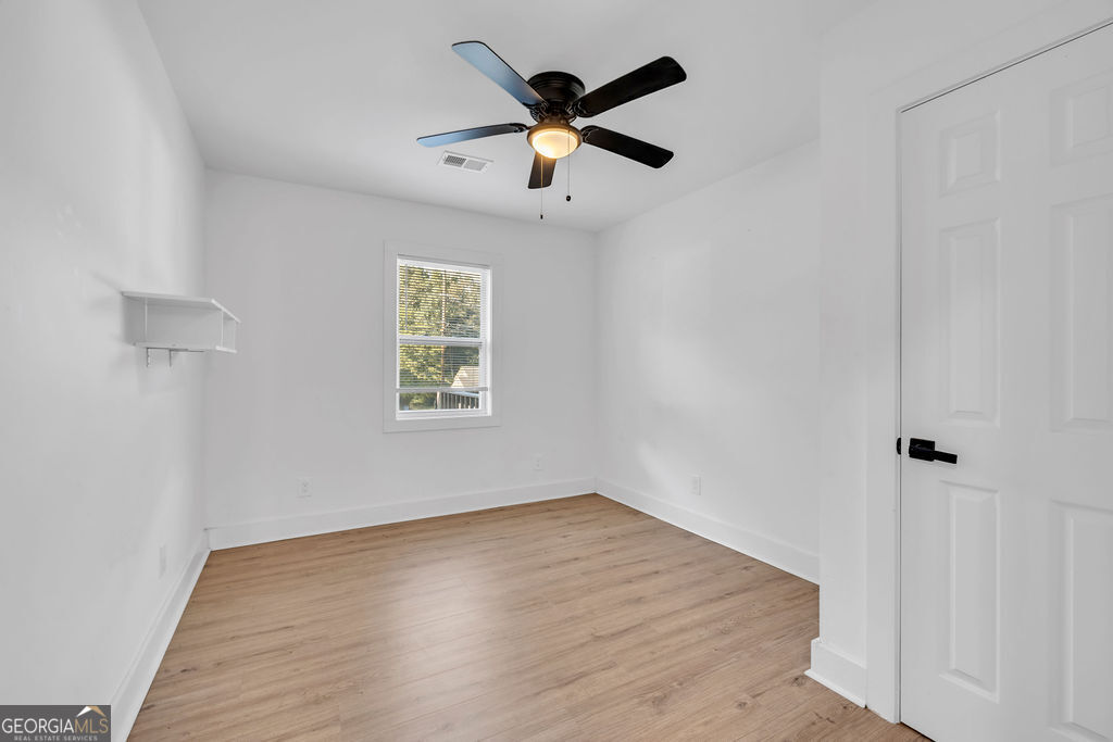 Empty room with light wood floors, a ceiling fan, and a window with blinds.