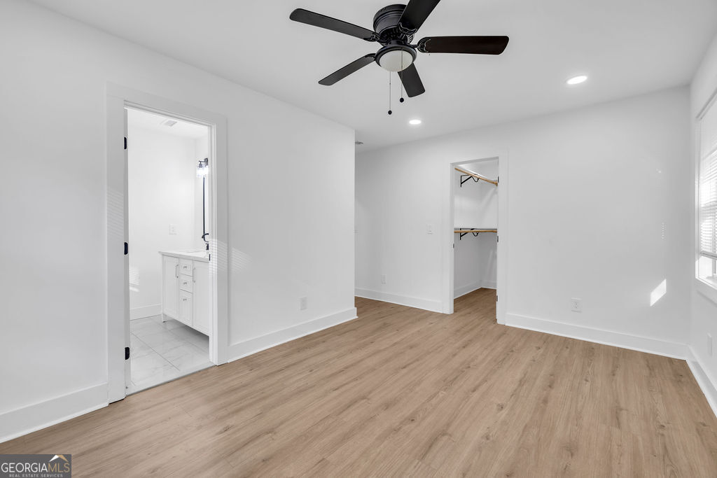 Empty bedroom with wood-look flooring, a black ceiling fan, and an open closet.