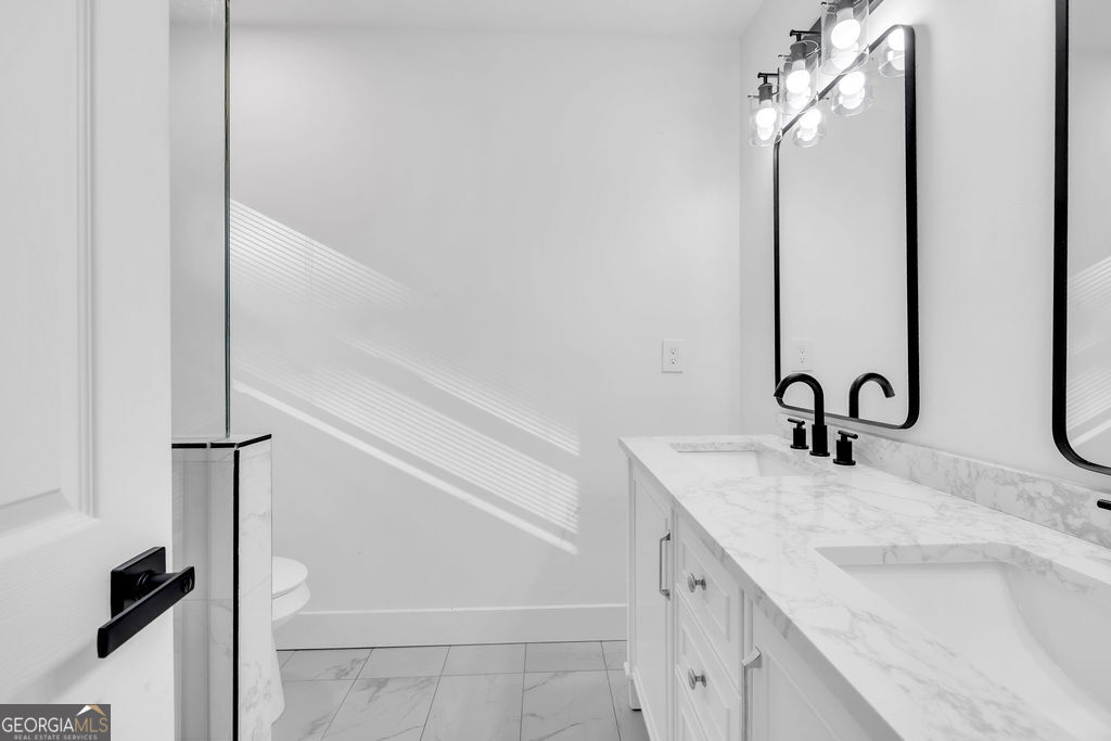 Bathroom with a marble-look vanity, black faucets, tall mirrors, and sunlight-striped walls.