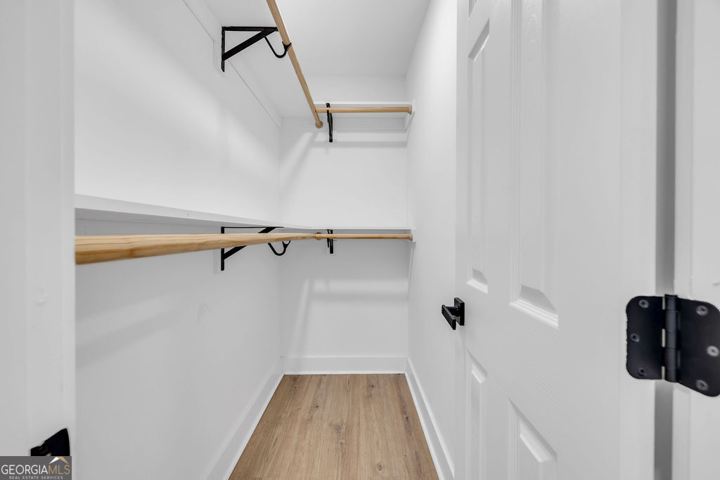 Walk-in closet with wooden hanging rods, shelves, and light wood-look flooring.