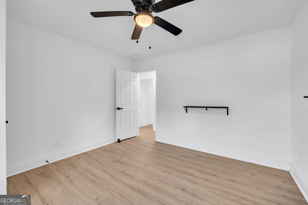 Empty room with light wood-look flooring, a ceiling fan, and a narrow wall-mounted shelf.