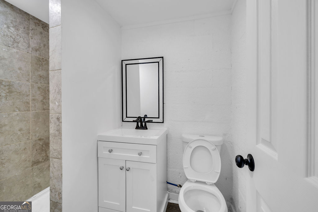 Bathroom with a white vanity, black-framed mirror, raised toilet seat, and beige tiled shower.