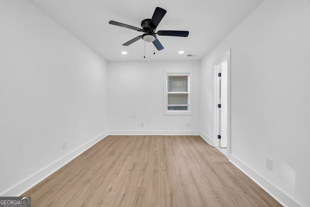 Empty room with light wood-look flooring, a black ceiling fan, and a window with blinds.