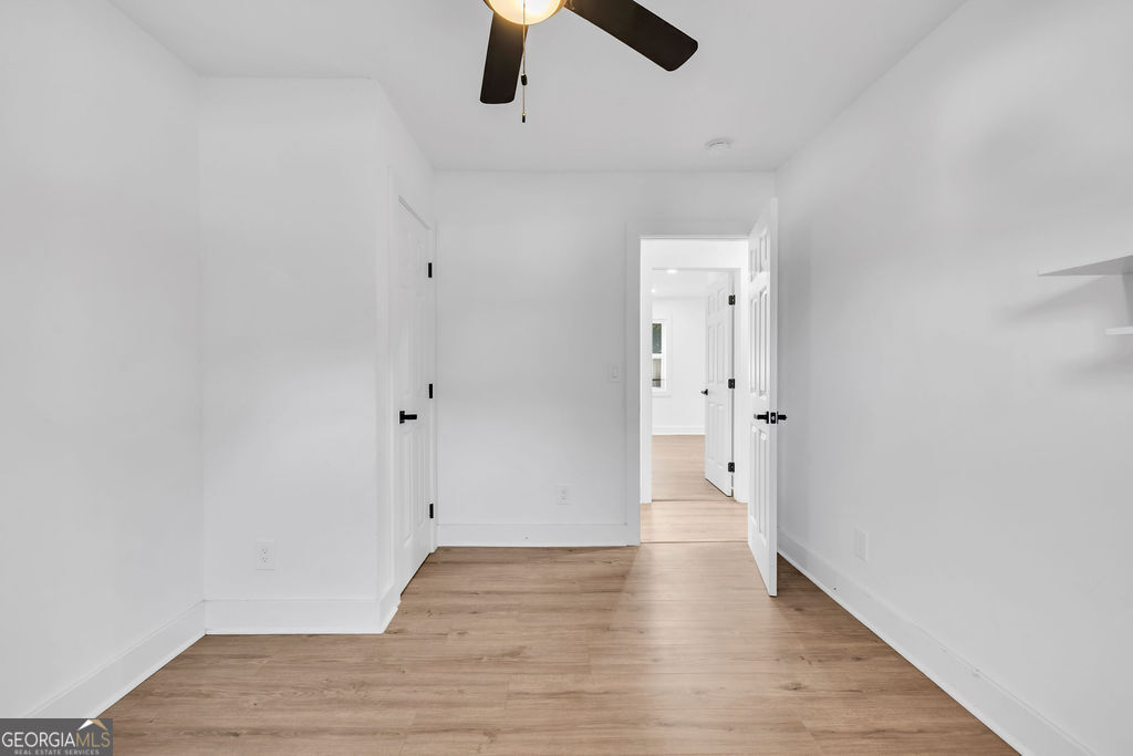 Empty bedroom with light wood flooring, a ceiling fan, and open doorways to adjoining rooms.