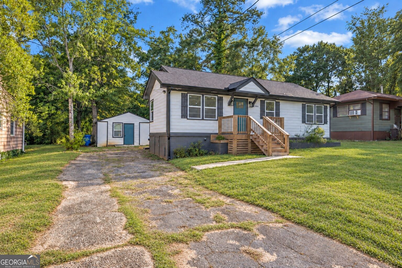 White single-story house with a blue door, wooden front steps, and a detached outbuilding beside the driveway.