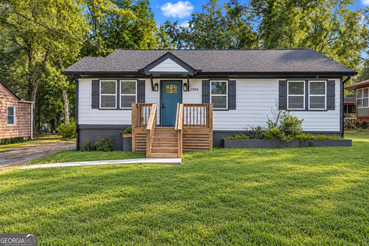 White single-story house with dark shutters, a blue door, and wooden front steps.