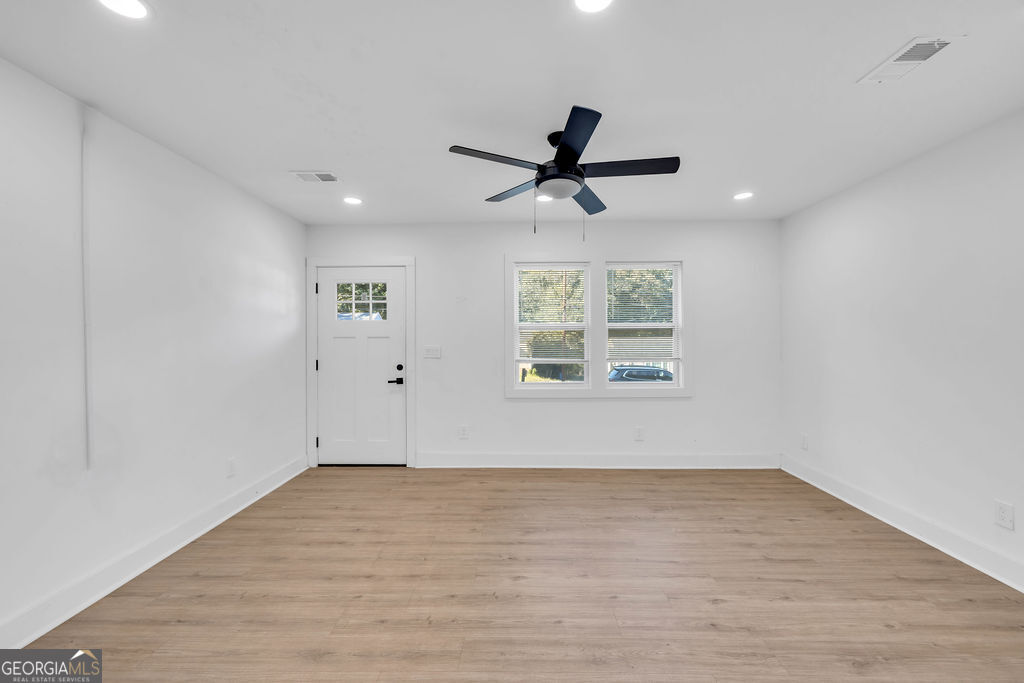 Vacant room with light wood floors, a dark ceiling fan, and two windows with blinds.