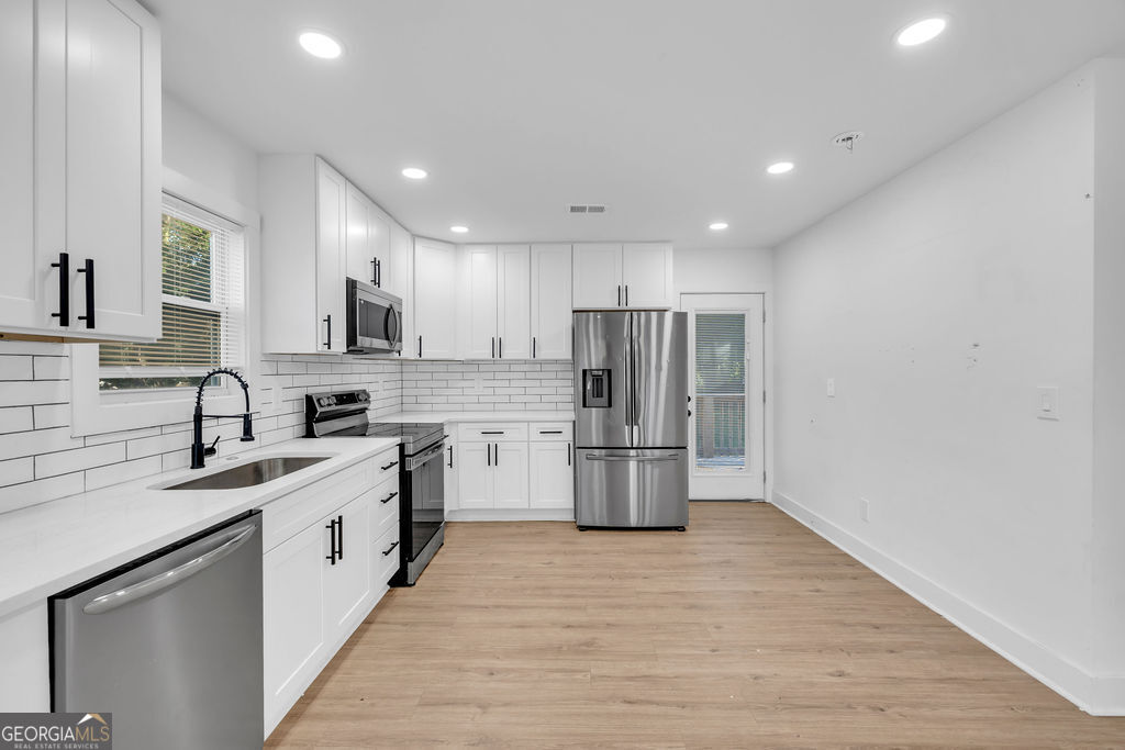 Kitchen with white cabinets, stainless steel appliances, subway tile backsplash, and light wood-look flooring.