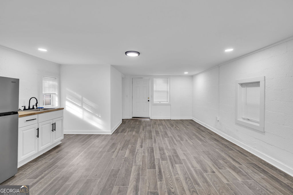 Vacant room with a small kitchenette, gray plank flooring, and windows along the white walls.