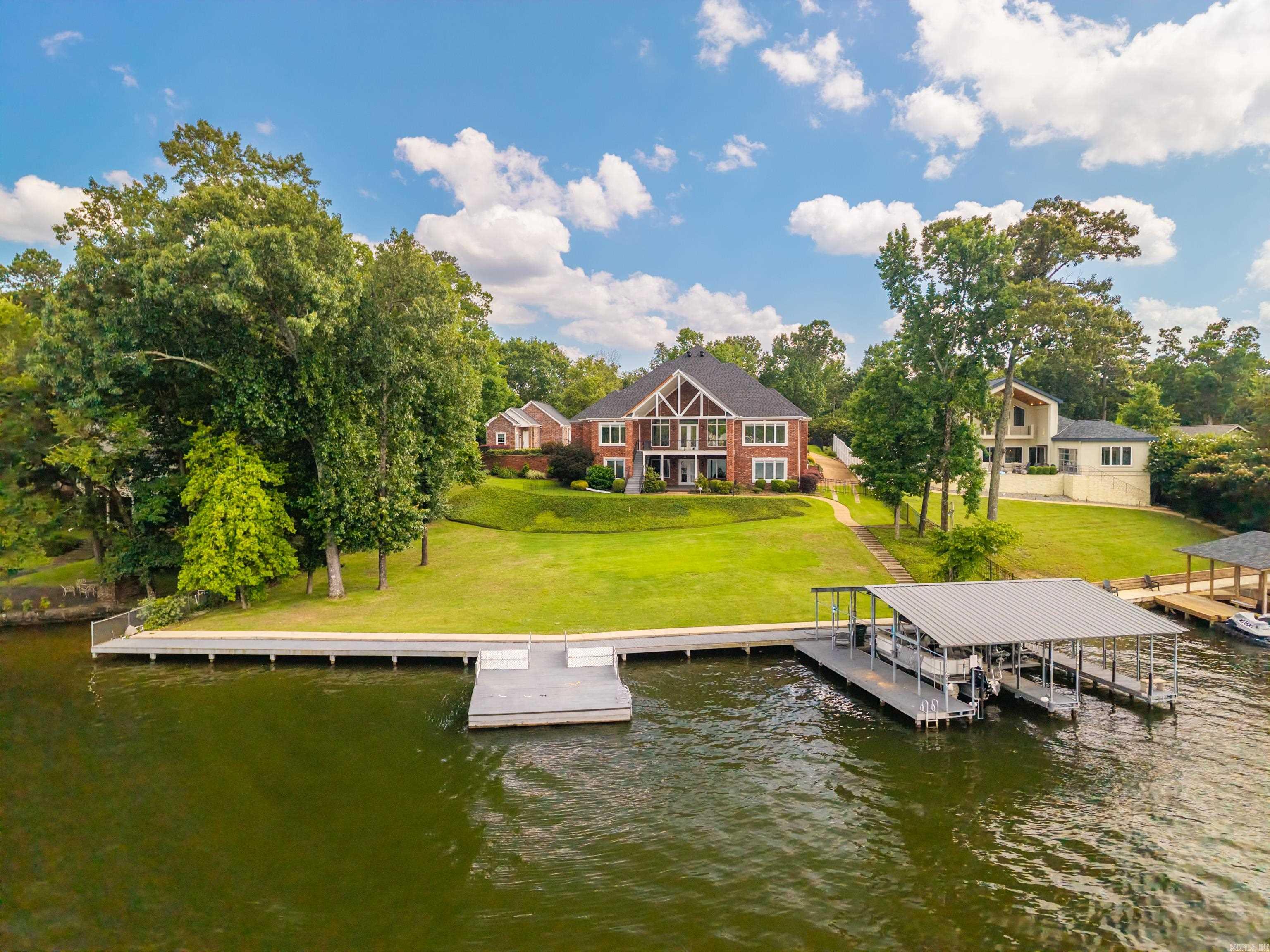 Aerial view of a brick waterfront home with a broad lawn and covered dock.