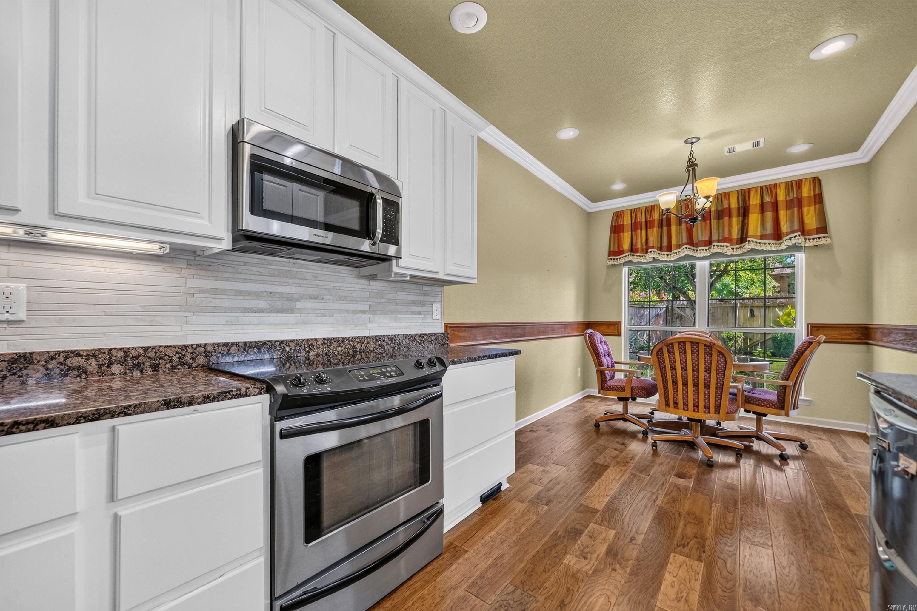 Kitchen with white cabinets and stainless appliances opening to a dining nook beside a large window.