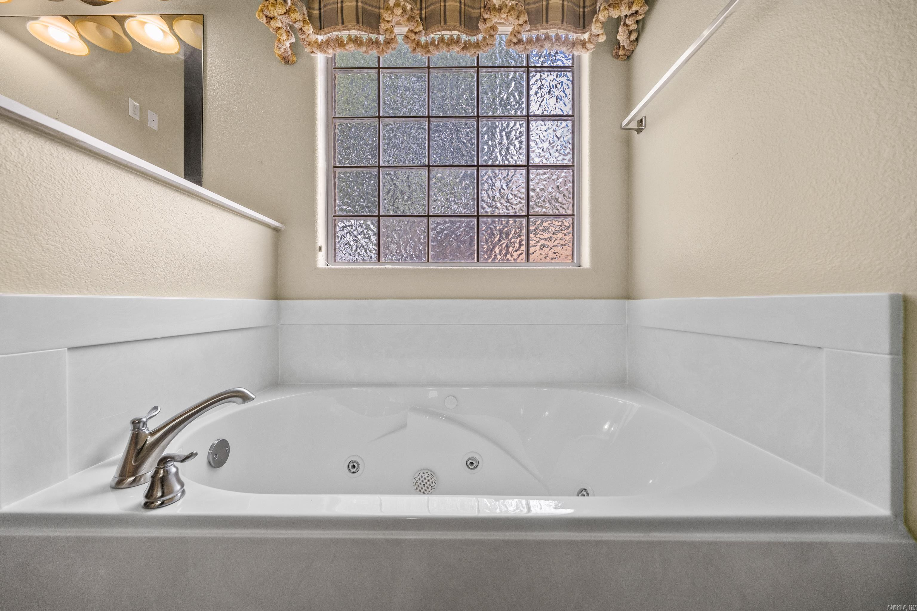 Bathroom jetted tub beneath a tall glass-block window, with white tile surround and chrome fixtures.