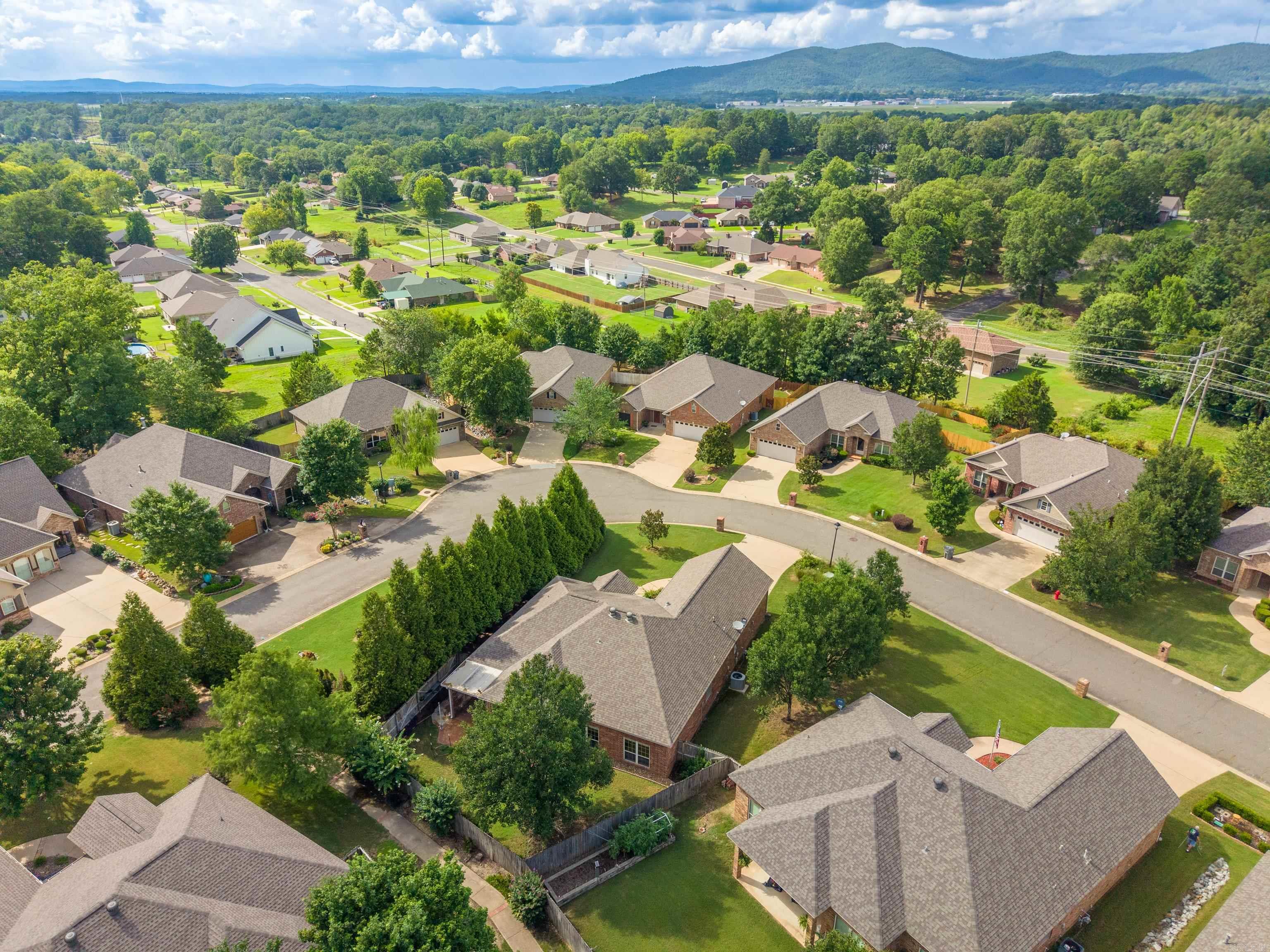 Aerial view of a leafy neighborhood with a curving street and wooded hills in the distance.
