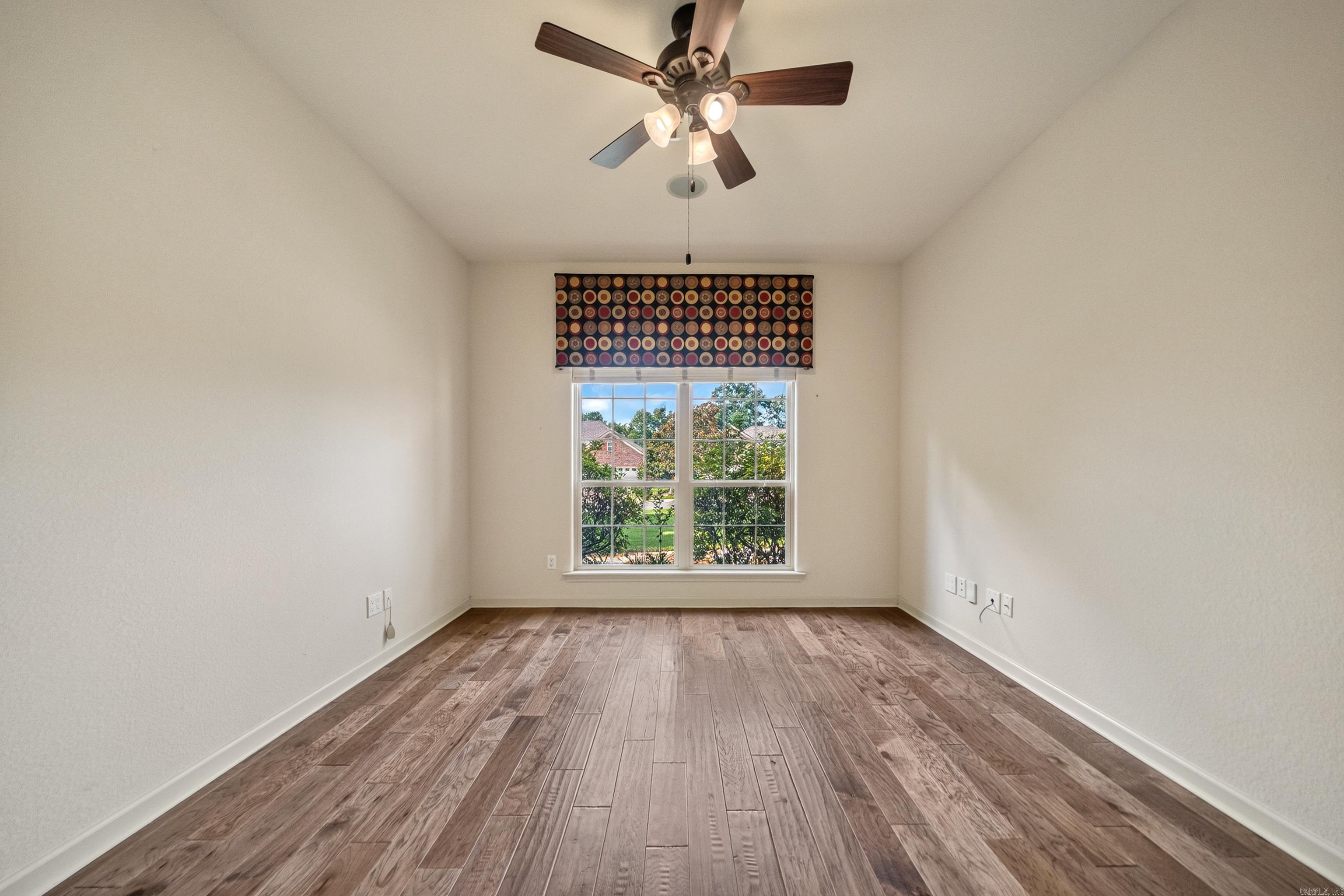 Empty room with wood-look plank flooring, a ceiling fan, and a window with a patterned valance.
