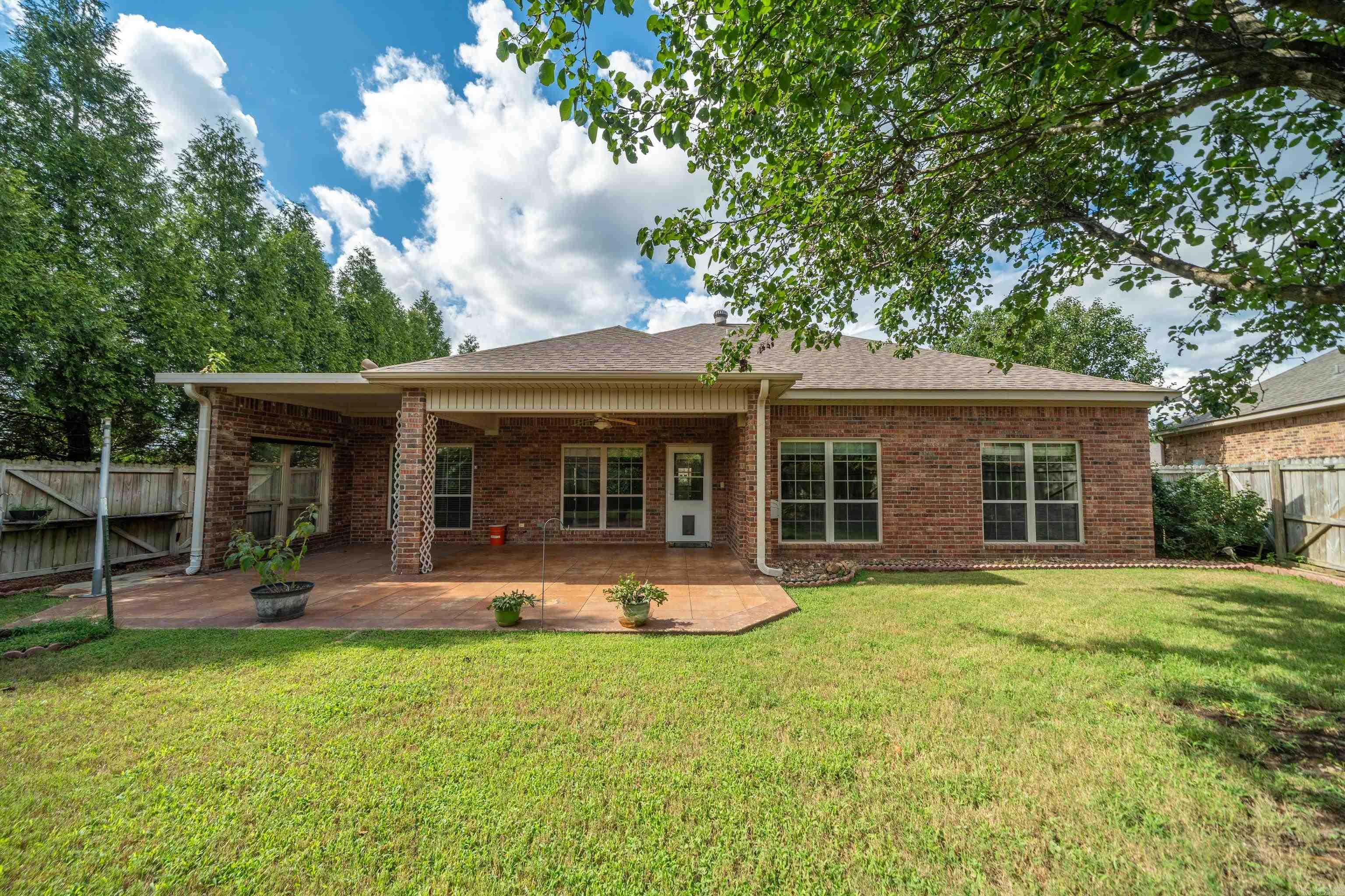 Rear of a brick home with a covered patio and spacious grassy backyard.