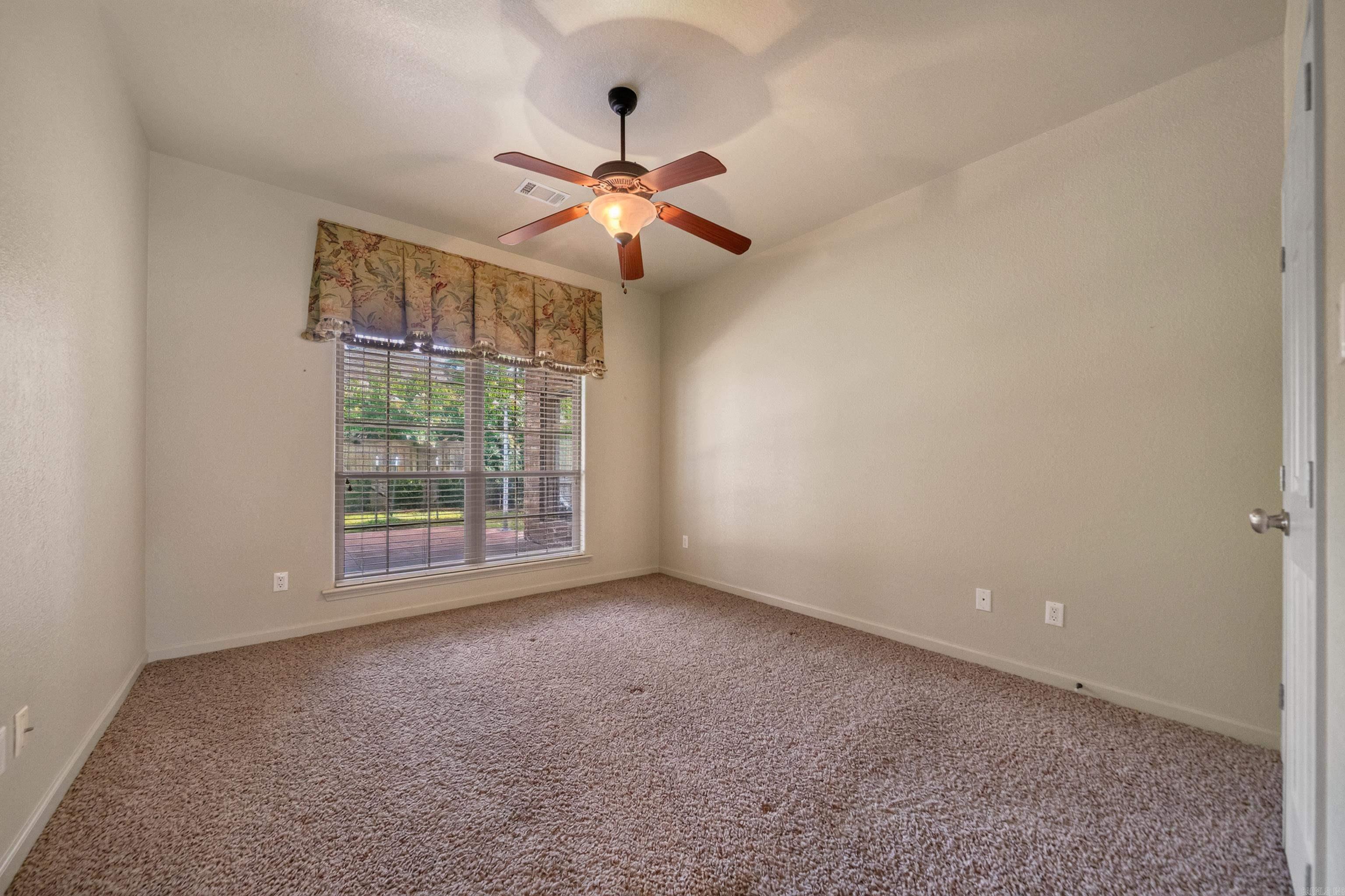 Unfurnished bedroom with brown carpet, a ceiling fan, and a large window with blinds.