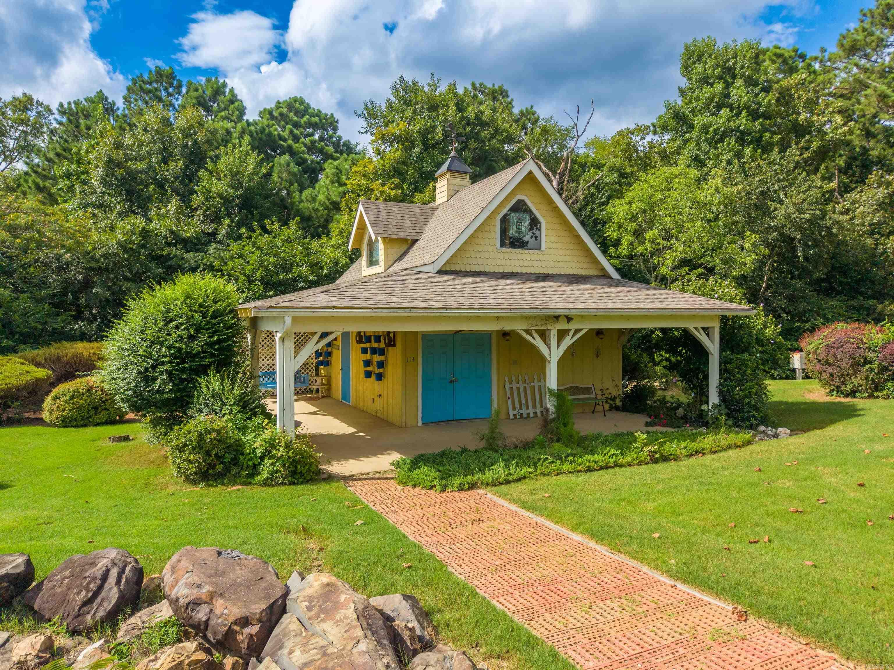 Yellow gabled building with blue doors, a covered porch, landscaped lawn, and brick walkway.