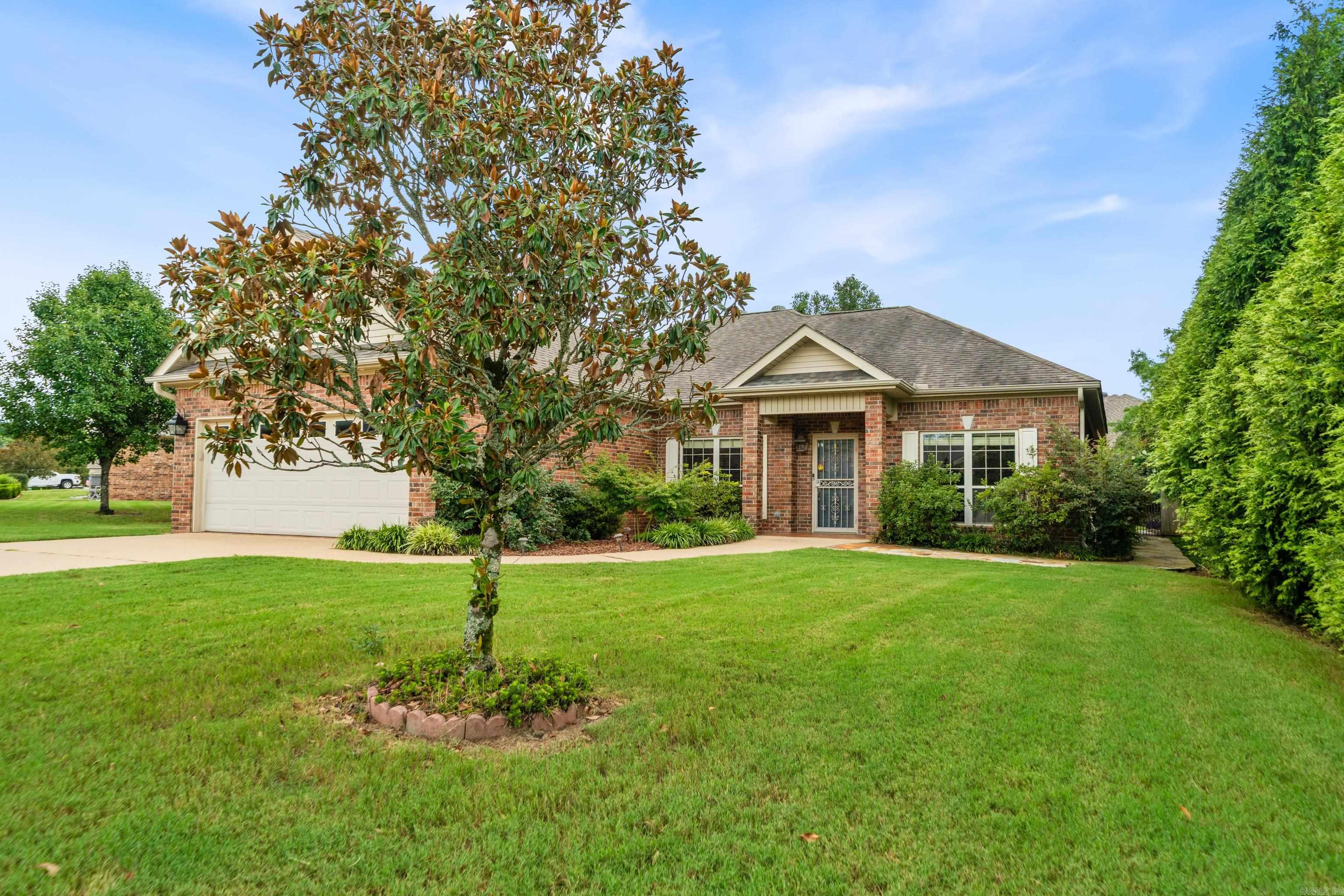 Brick home with an attached garage and broad green lawn, partly screened by a mature tree.