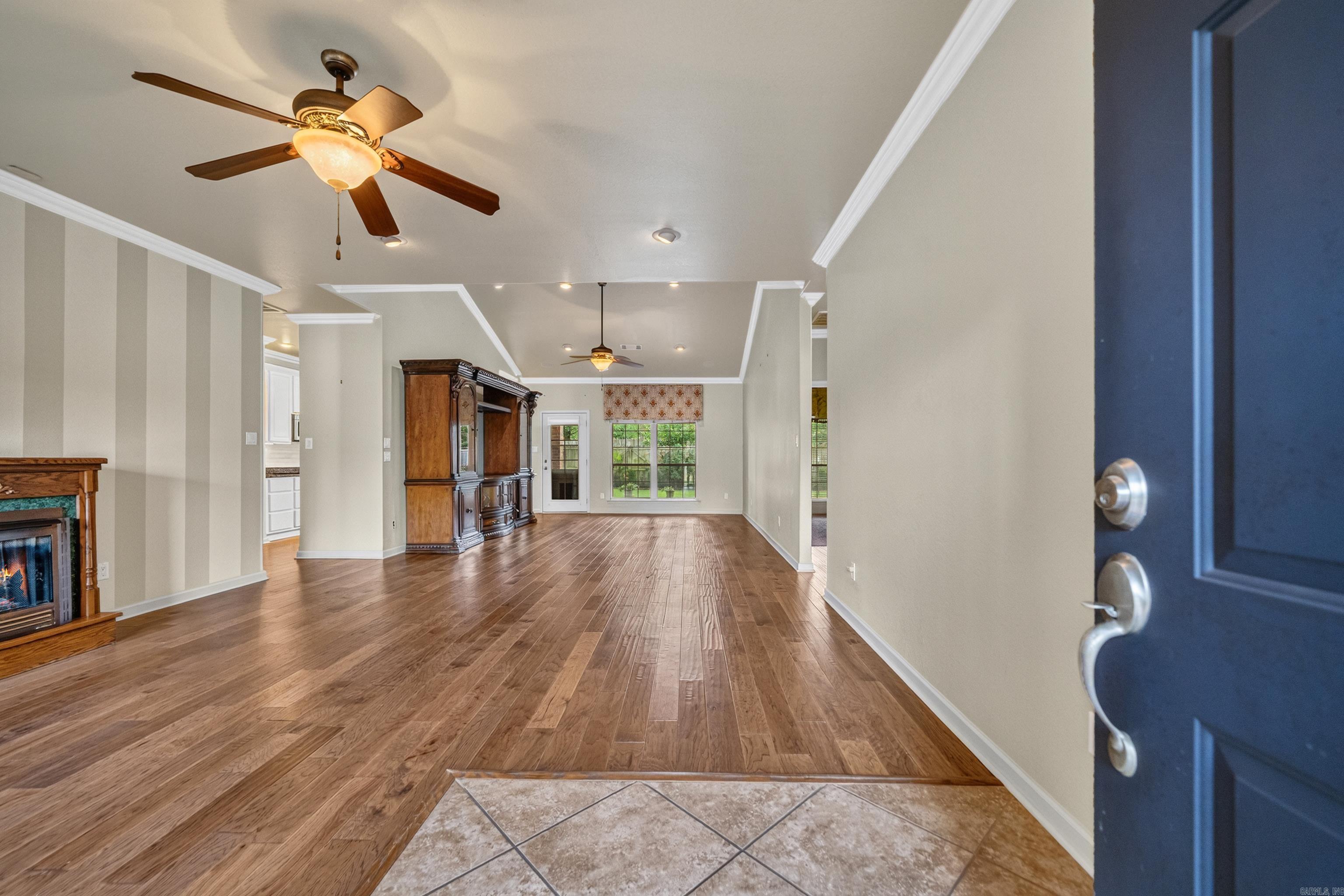 Open living room with hardwood floors, a fireplace, and ceiling fans, viewed from the entry.