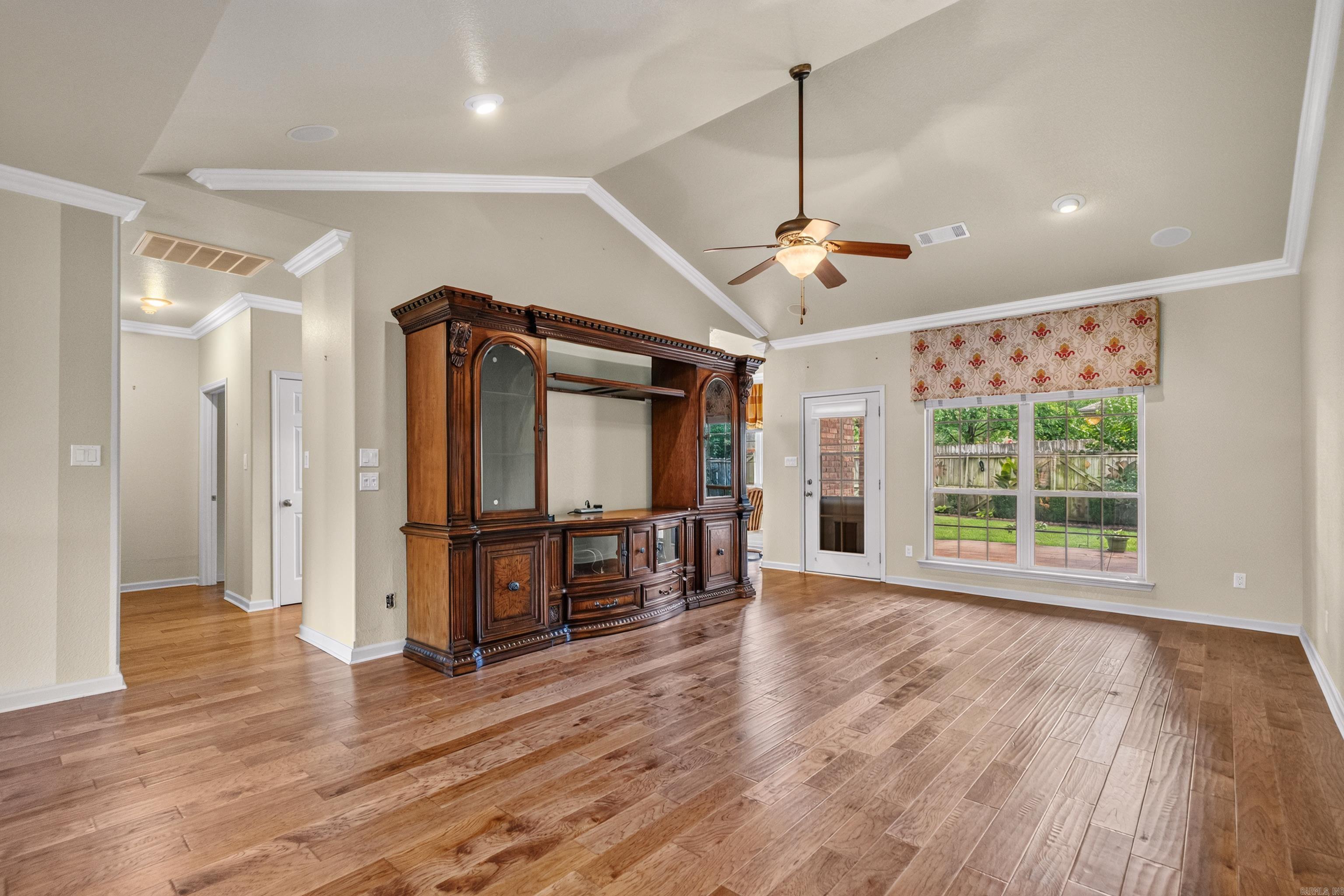 Living room with hardwood floors, an ornate entertainment cabinet, and windows overlooking a fenced backyard.