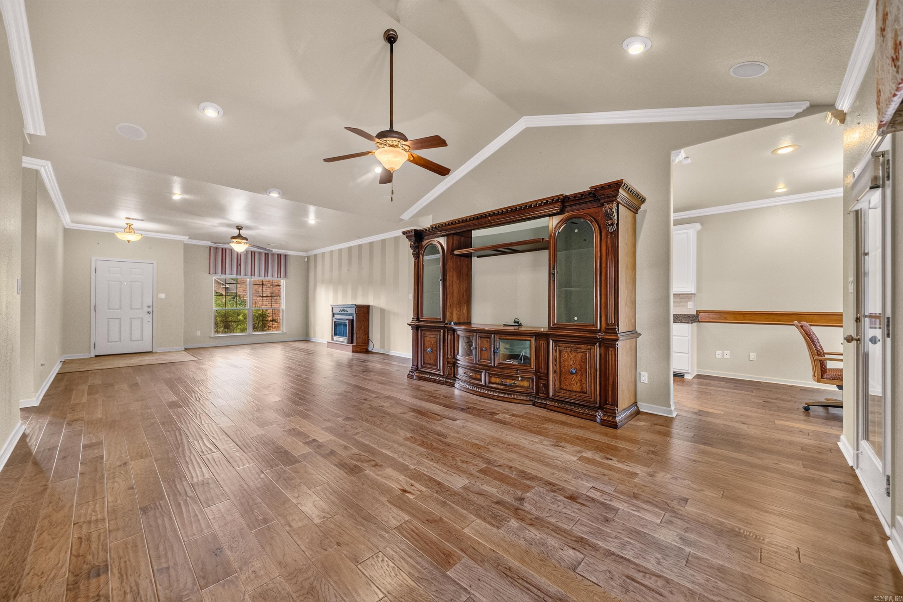 Living room with wood-look floors, vaulted ceiling, and ornate wooden entertainment center.