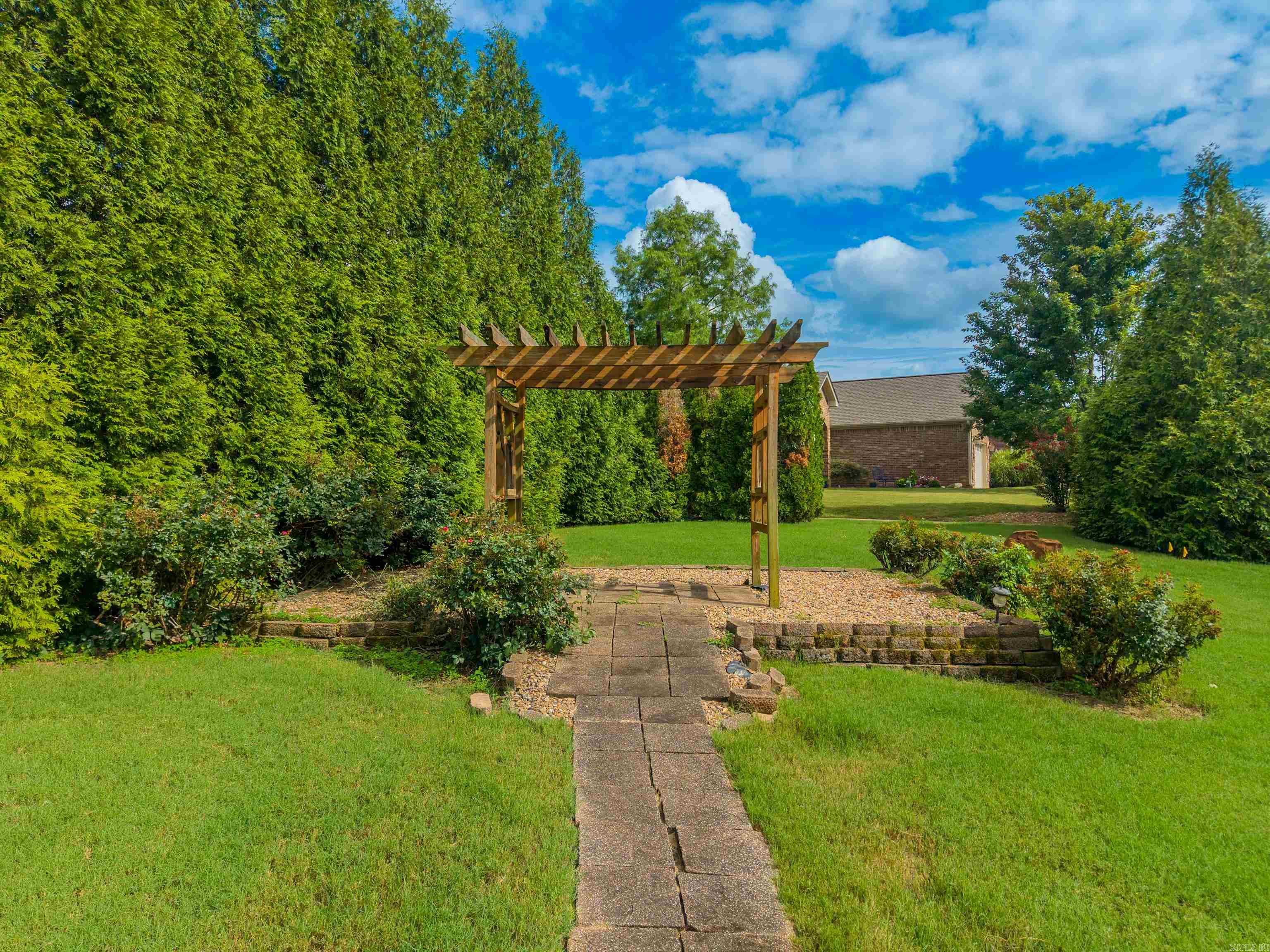 Backyard with a stone path leading to a wooden pergola amid hedges and lawn.