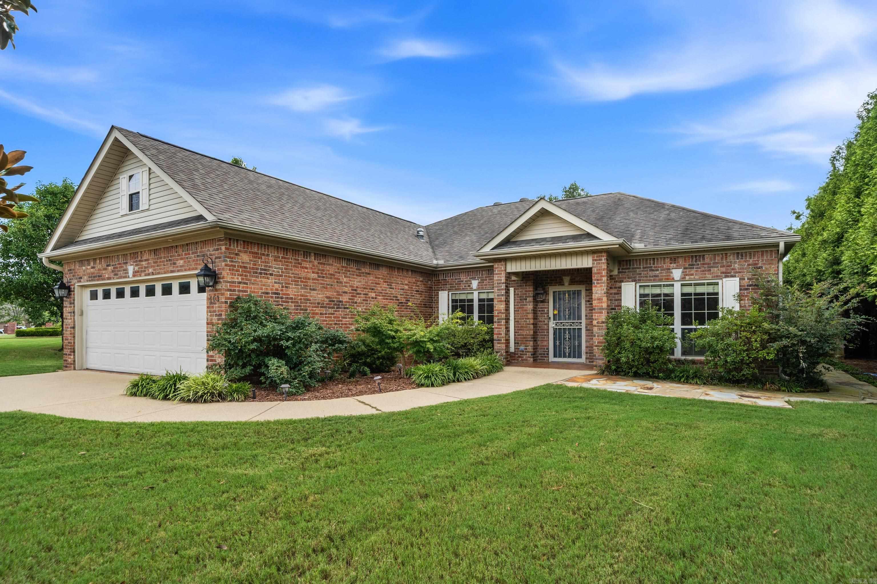 Red-brick home with a white garage, covered entry, and landscaped front lawn.