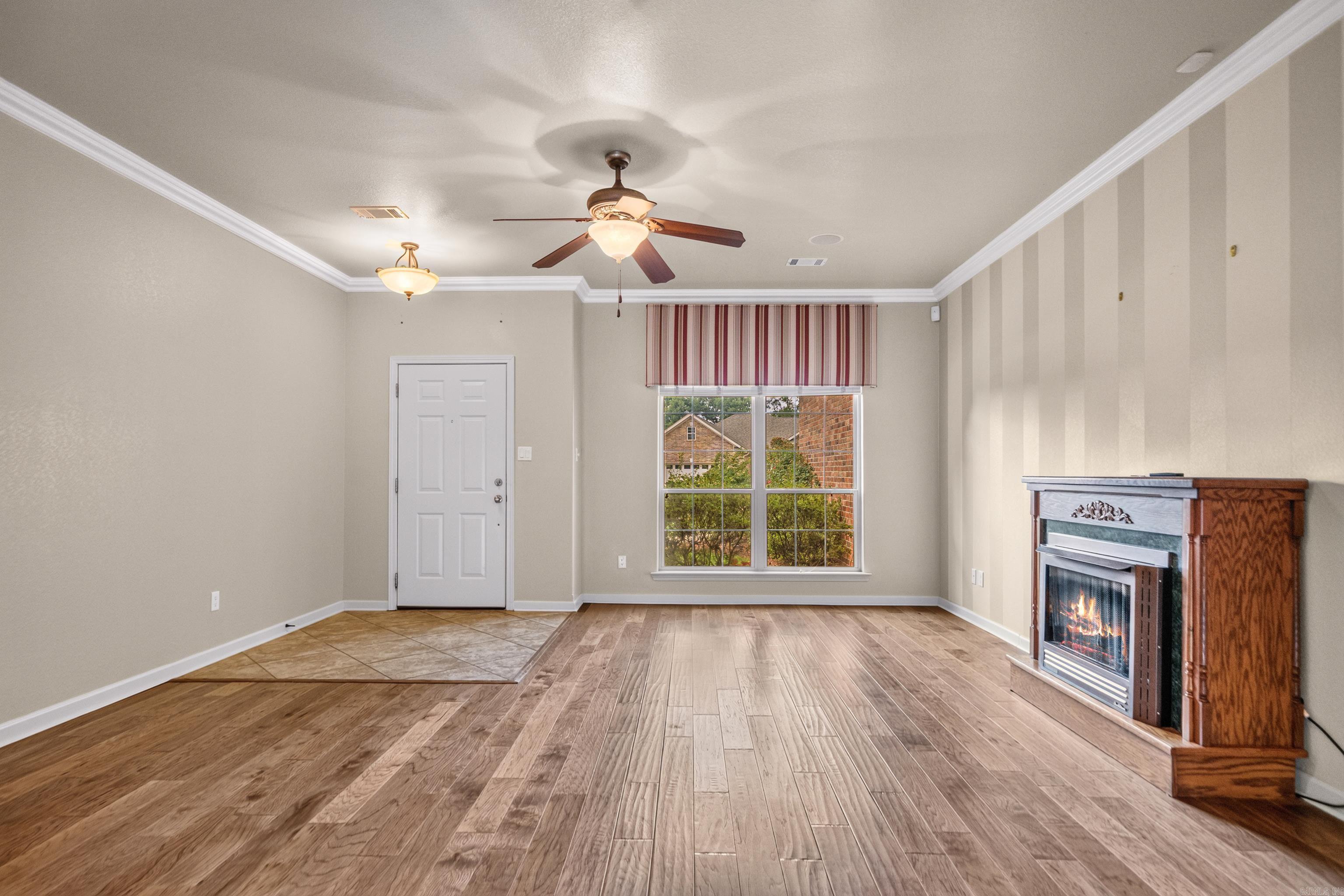 Empty living room with wood-look floors, a large window, and a lit fireplace.