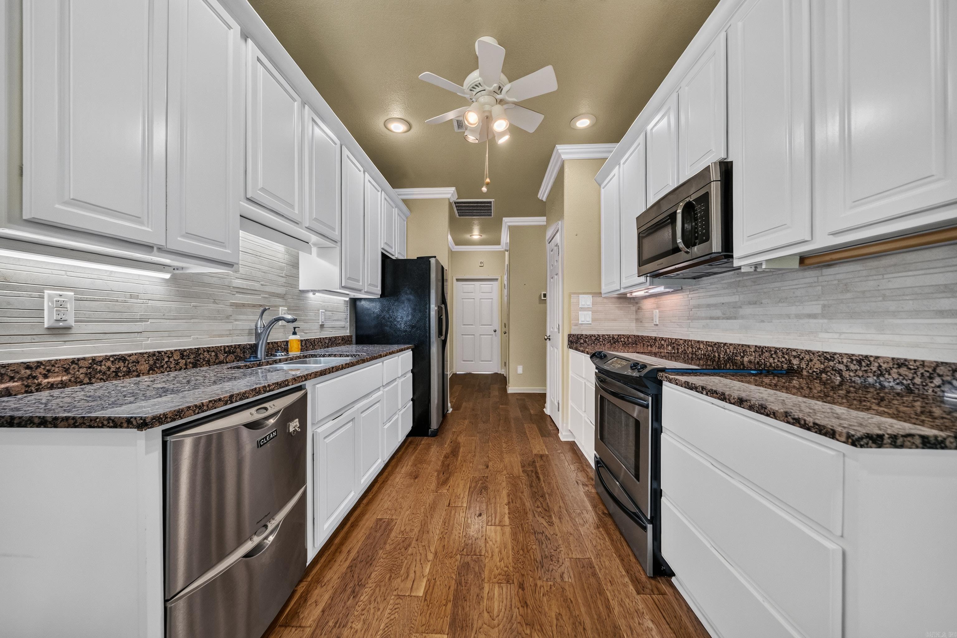 Kitchen with white cabinets, granite counters, stainless steel appliances, and wood-look flooring.
