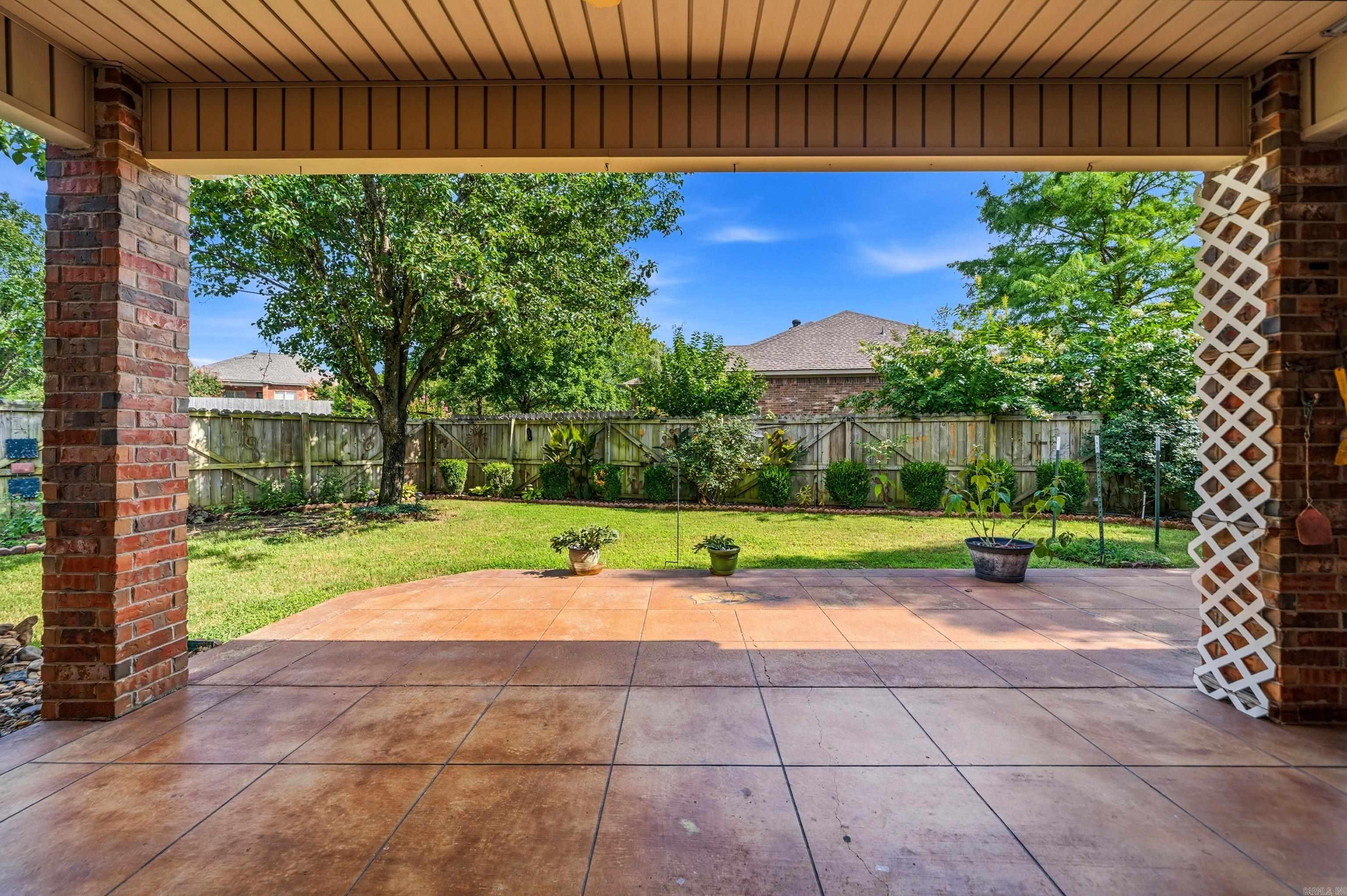 Covered concrete patio overlooking a fenced lawn with mature trees and shrubs.