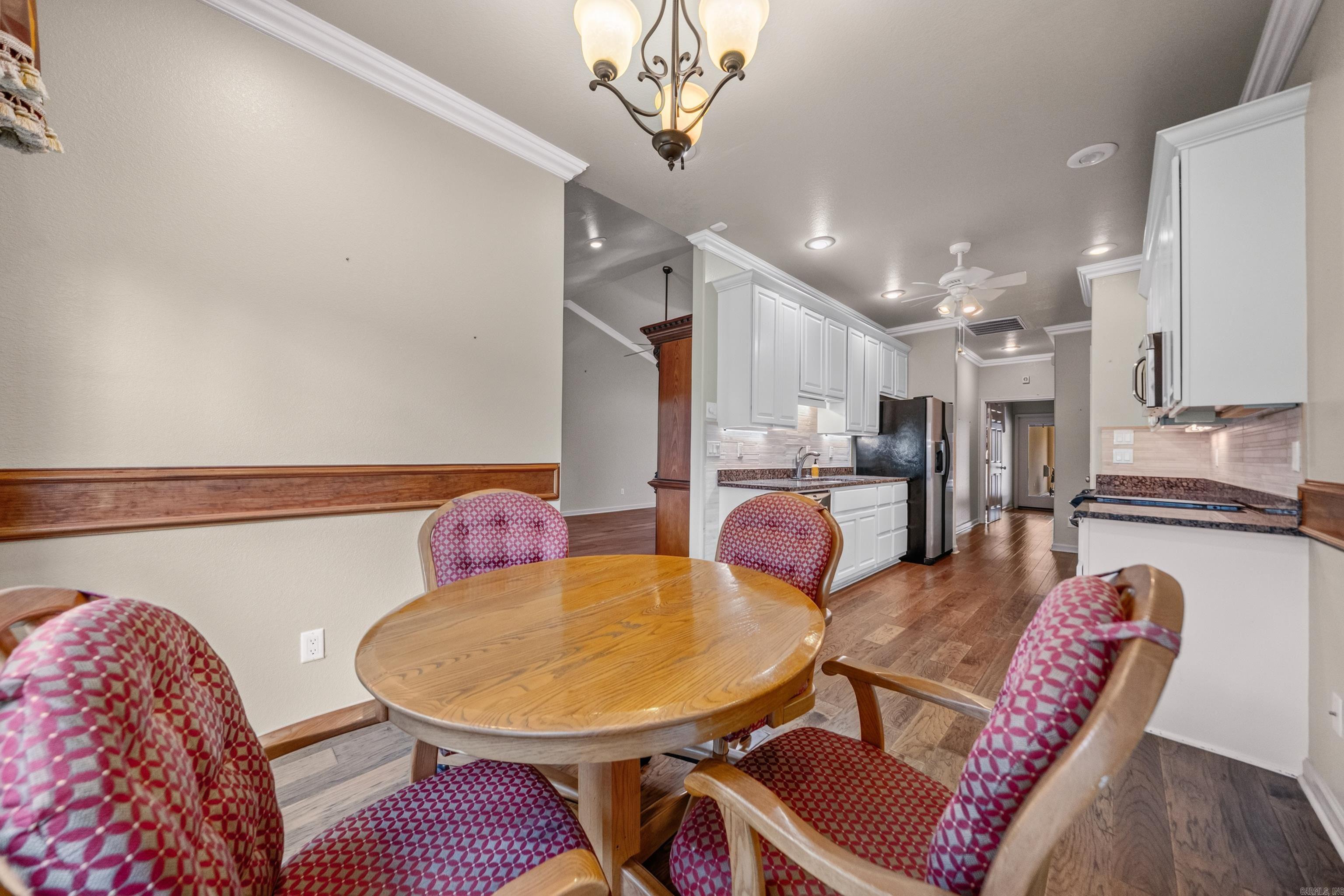 Dining area with a round wooden table and patterned chairs beside a long white-cabinet kitchen.