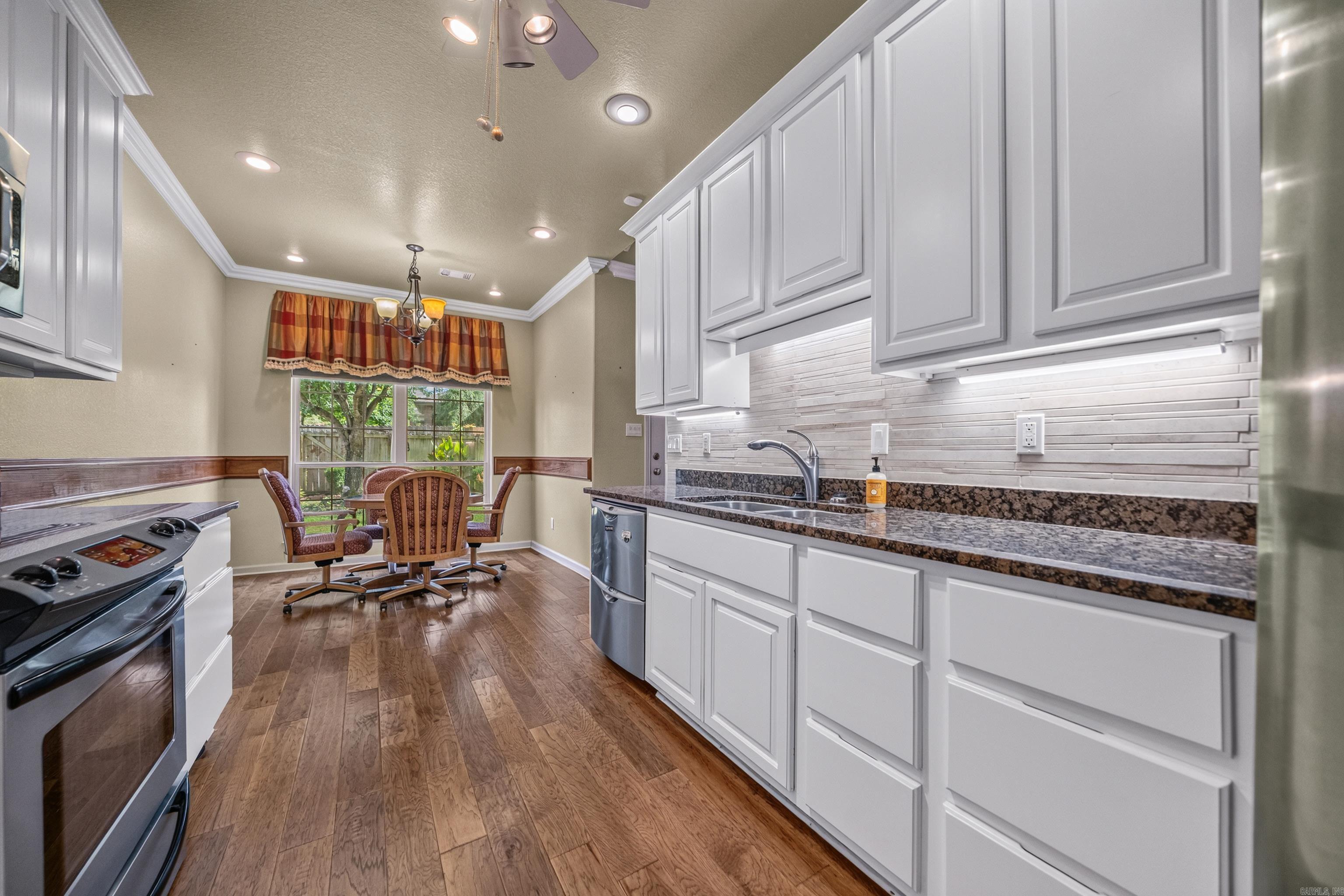 Kitchen with white cabinets, granite counters, wood-look flooring, and a dining table beside the window.