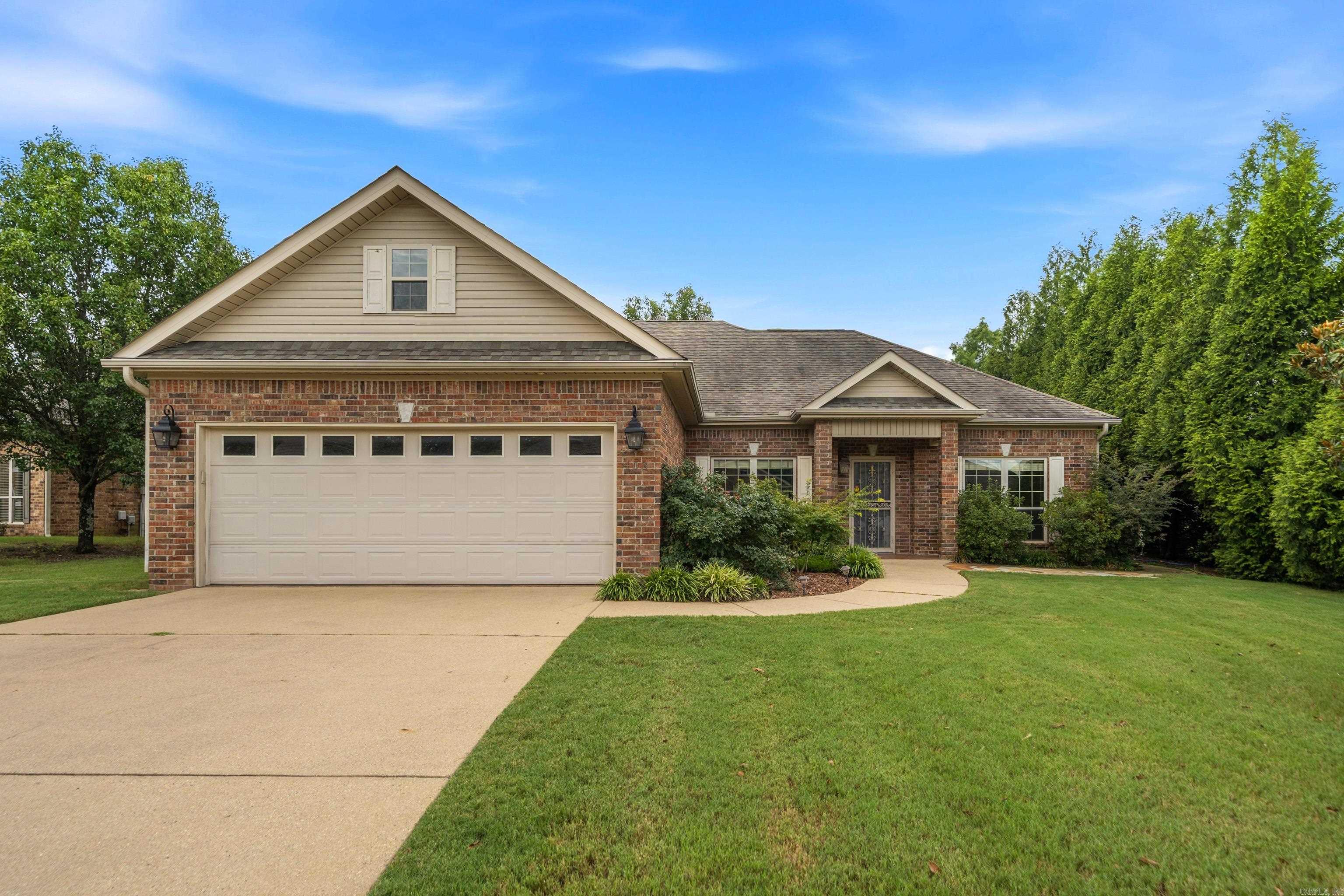 Brick house with beige gables, a two-car garage, landscaped shrubs, and a broad front lawn.