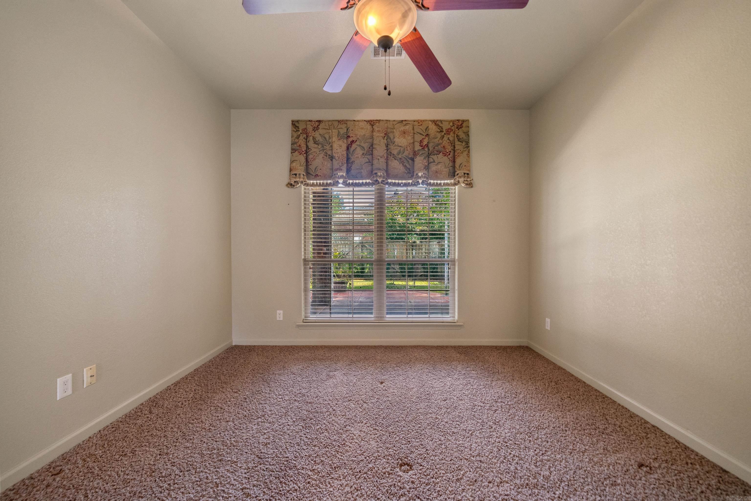 Empty carpeted bedroom with a floral window valance and ceiling fan.