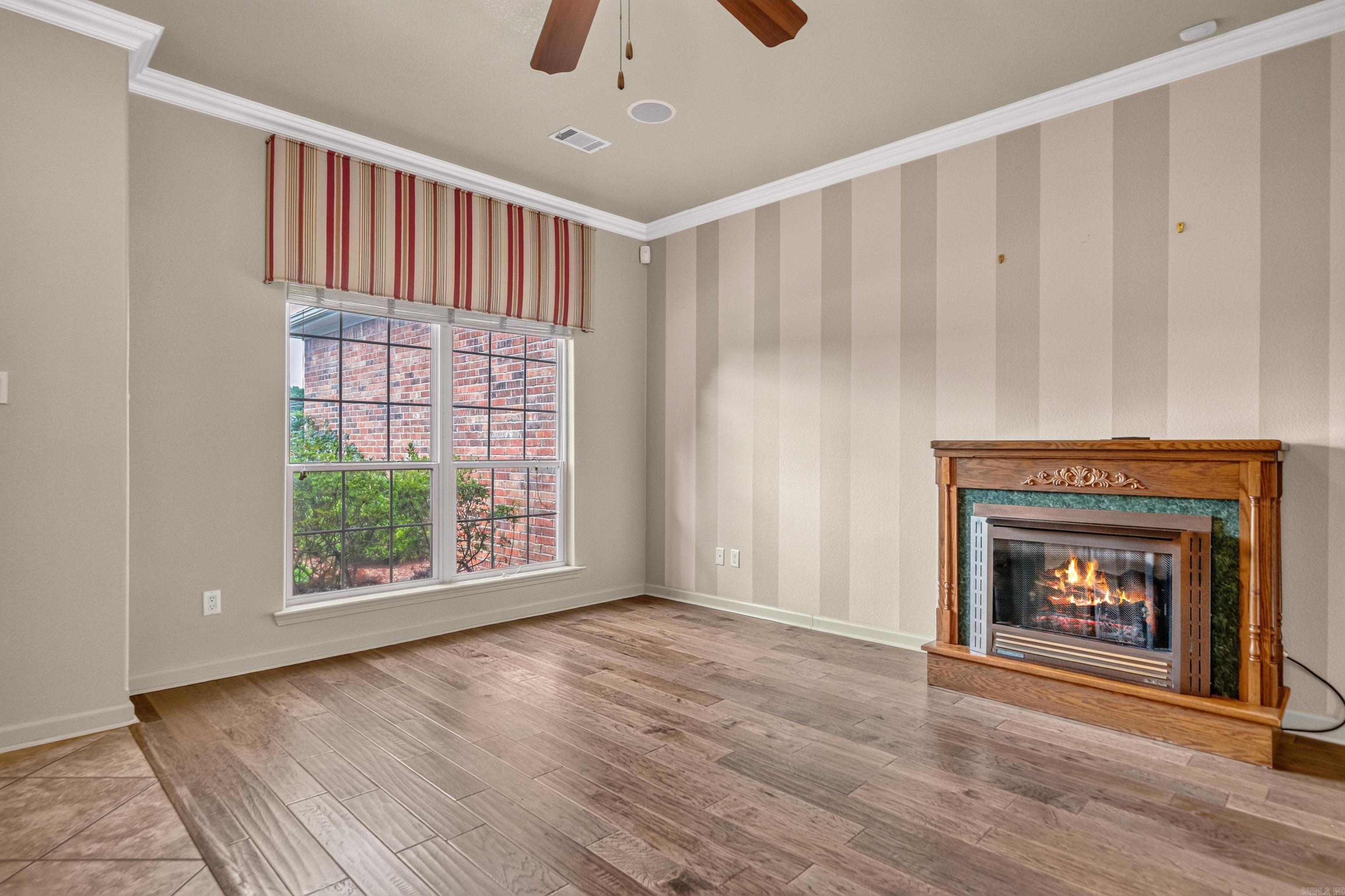 Empty living room with plank flooring, striped walls, a large window, and a wood-framed fireplace.