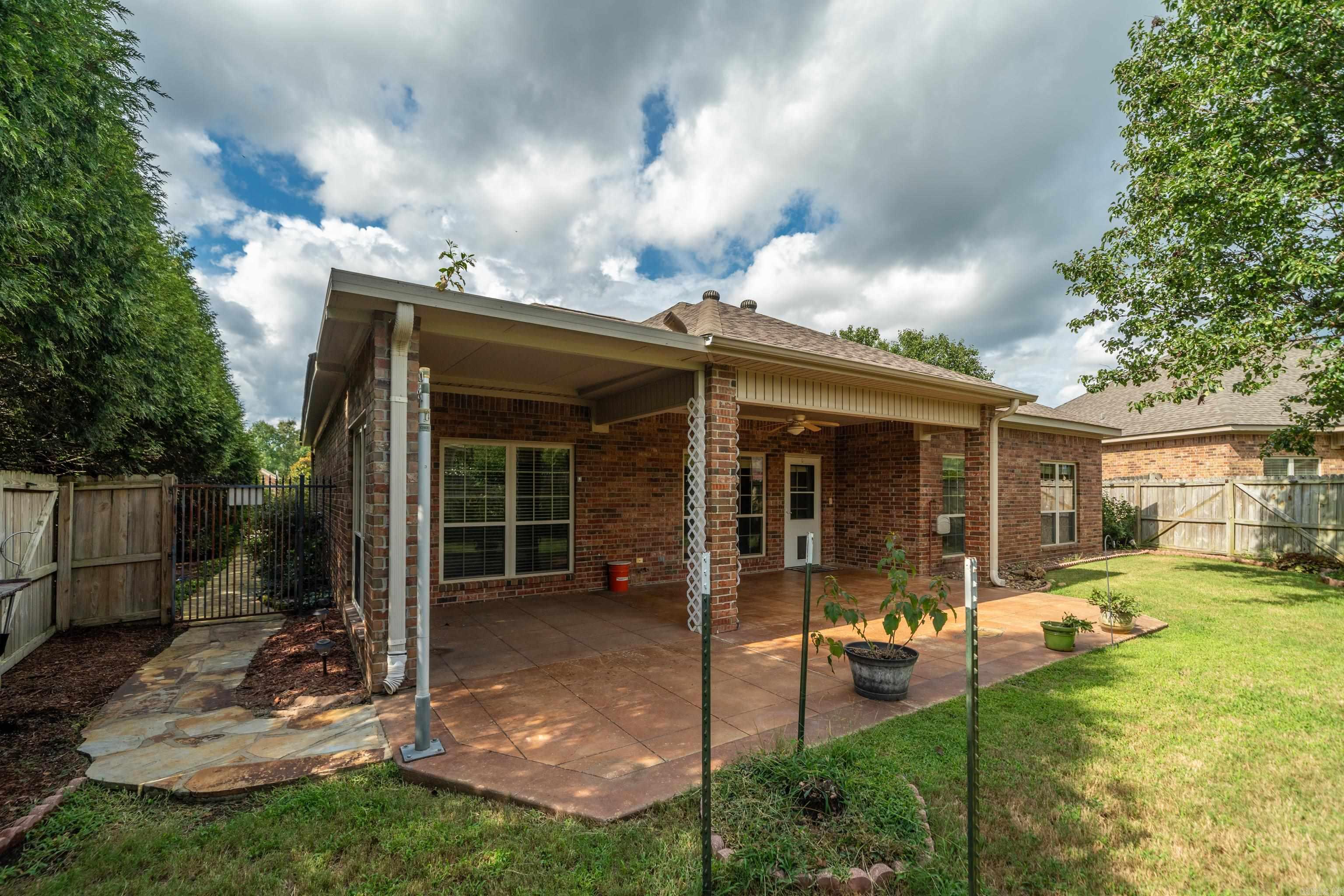 Brick home with a covered patio, potted plants, and a fenced grassy backyard.