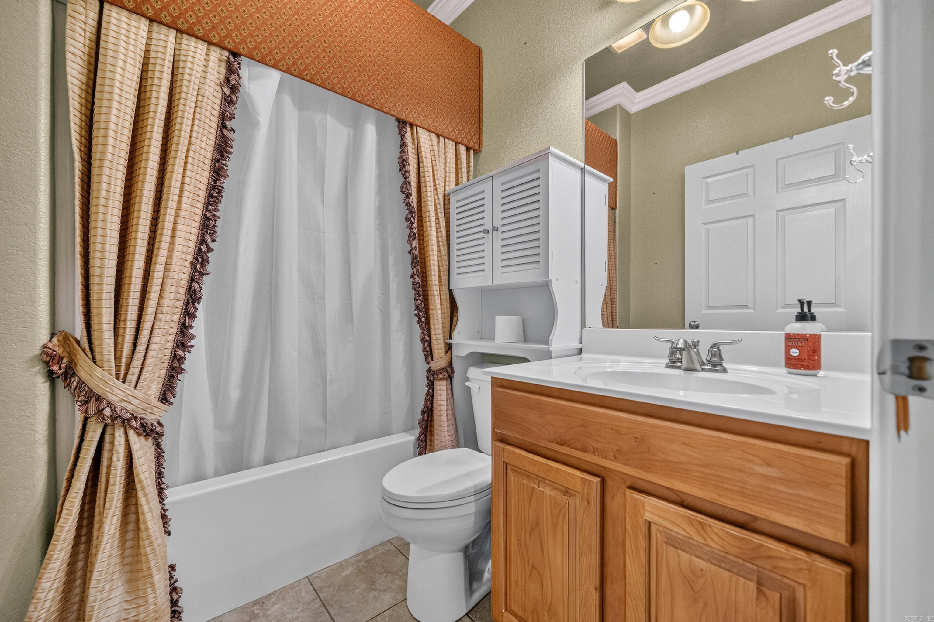 Bathroom with a wood vanity, white bathtub, toilet, and beige curtains.