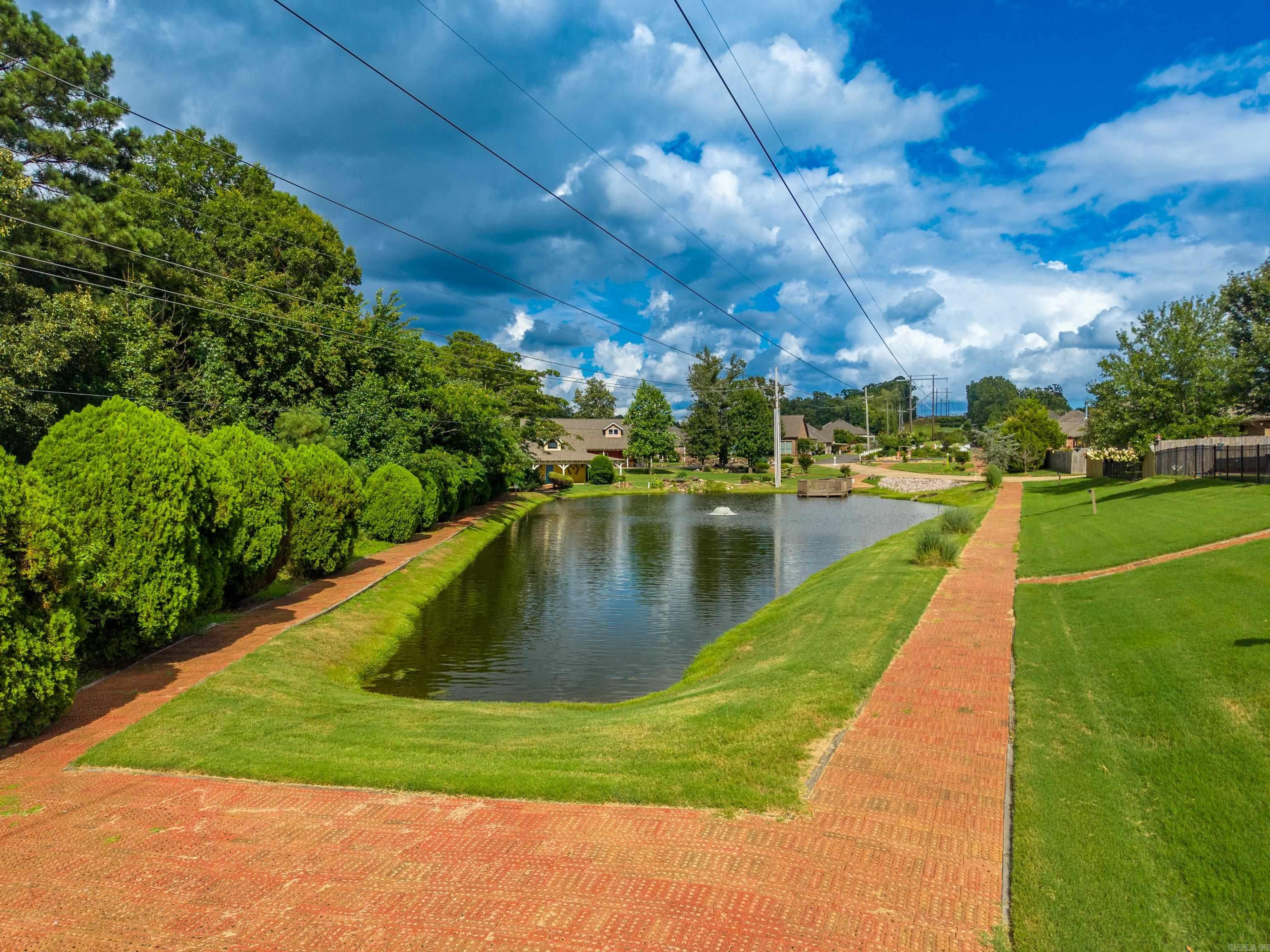 Landscaped community pond with a fountain, brick paths, and homes nearby.