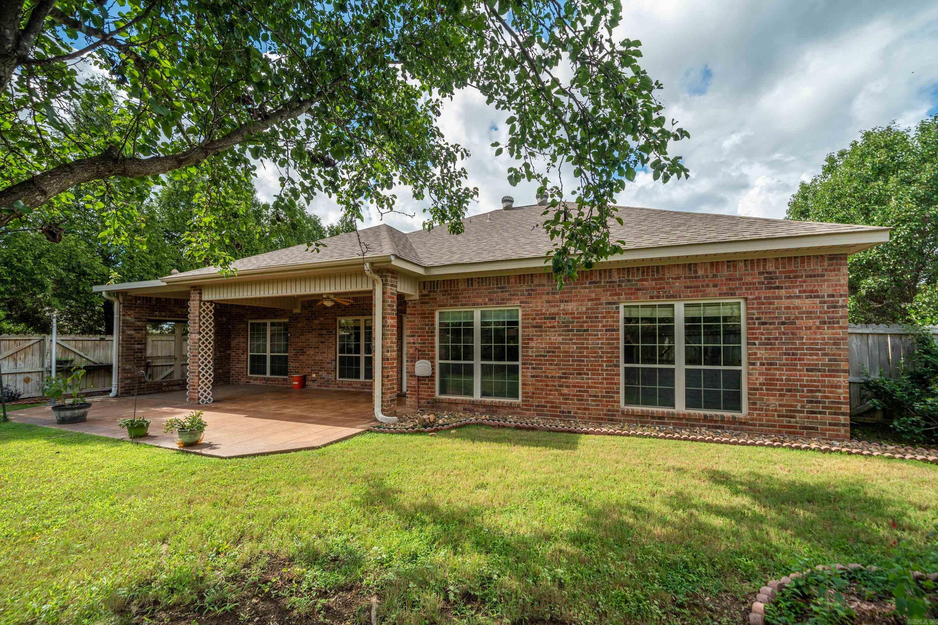 Red brick home with a covered patio and fenced grassy backyard.